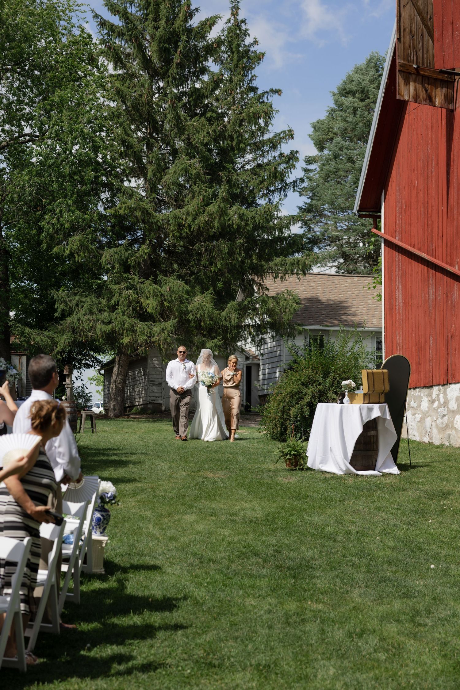 Outdoor wedding ceremony with red barn backdrop and white chairs on grass.