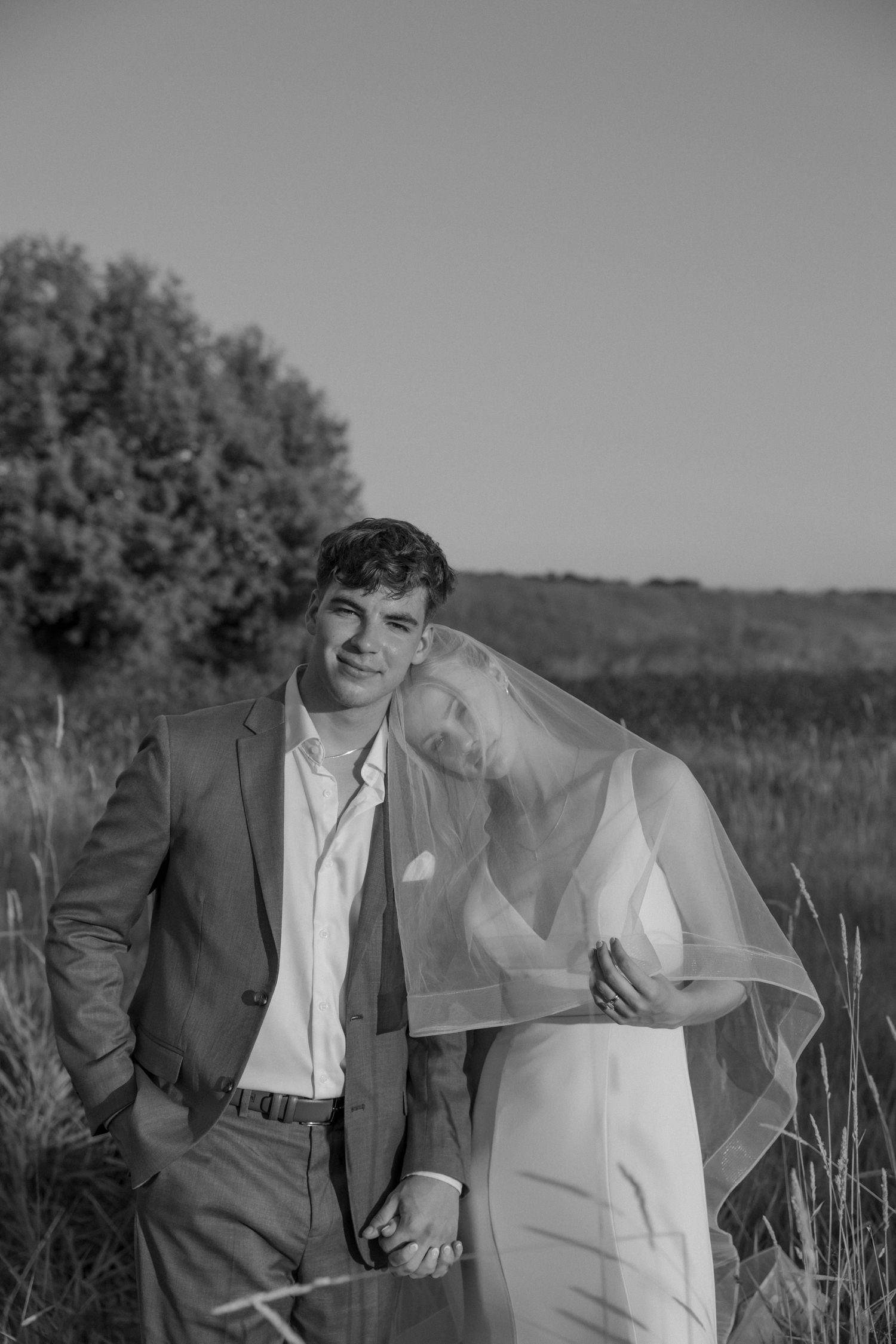 Black and white portrait of newlyweds laughing together in a field with long grass and natural lighting.
