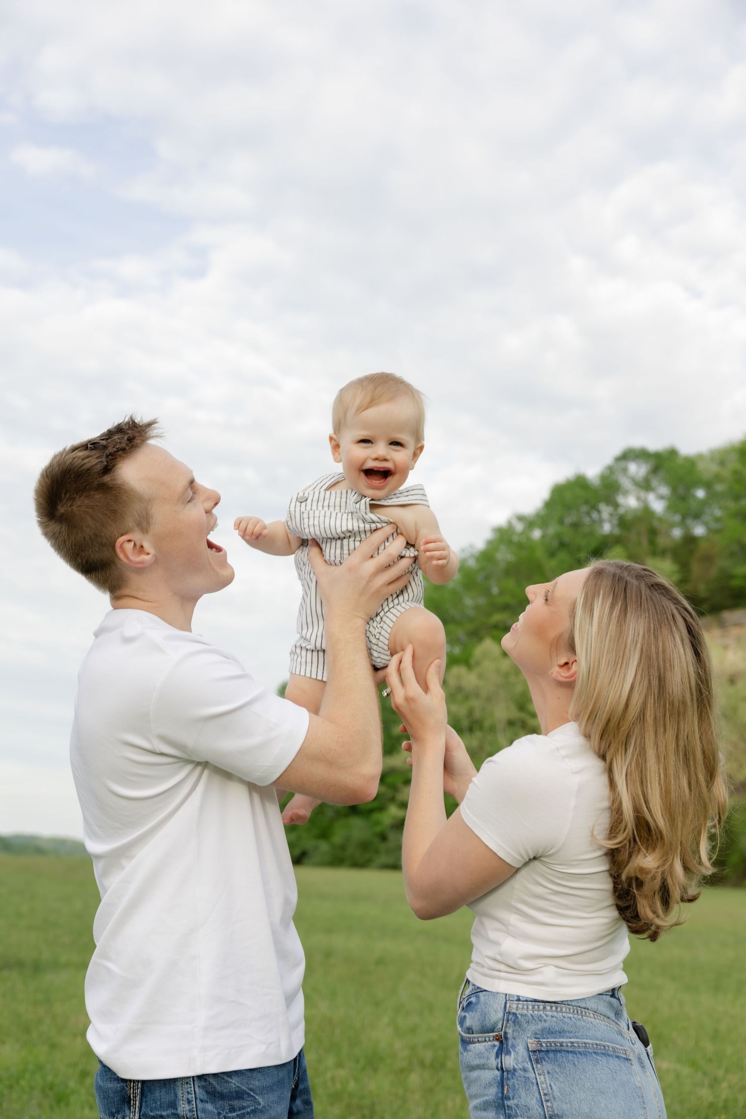 Parents playing with their baby outdoors in a sunny meadow landscape.