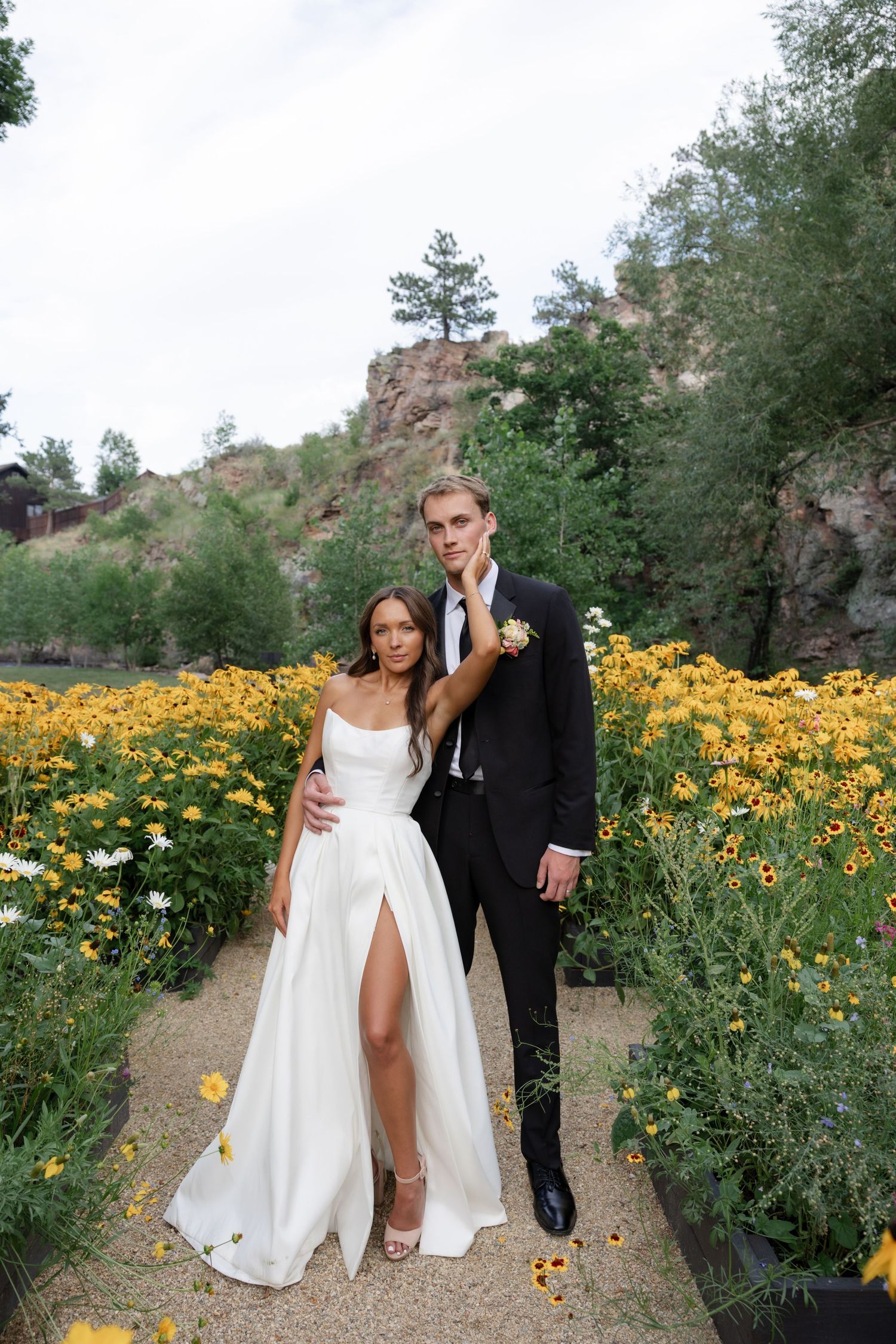 A couple poses together in a field of vibrant yellow wildflowers along a mountain trail.