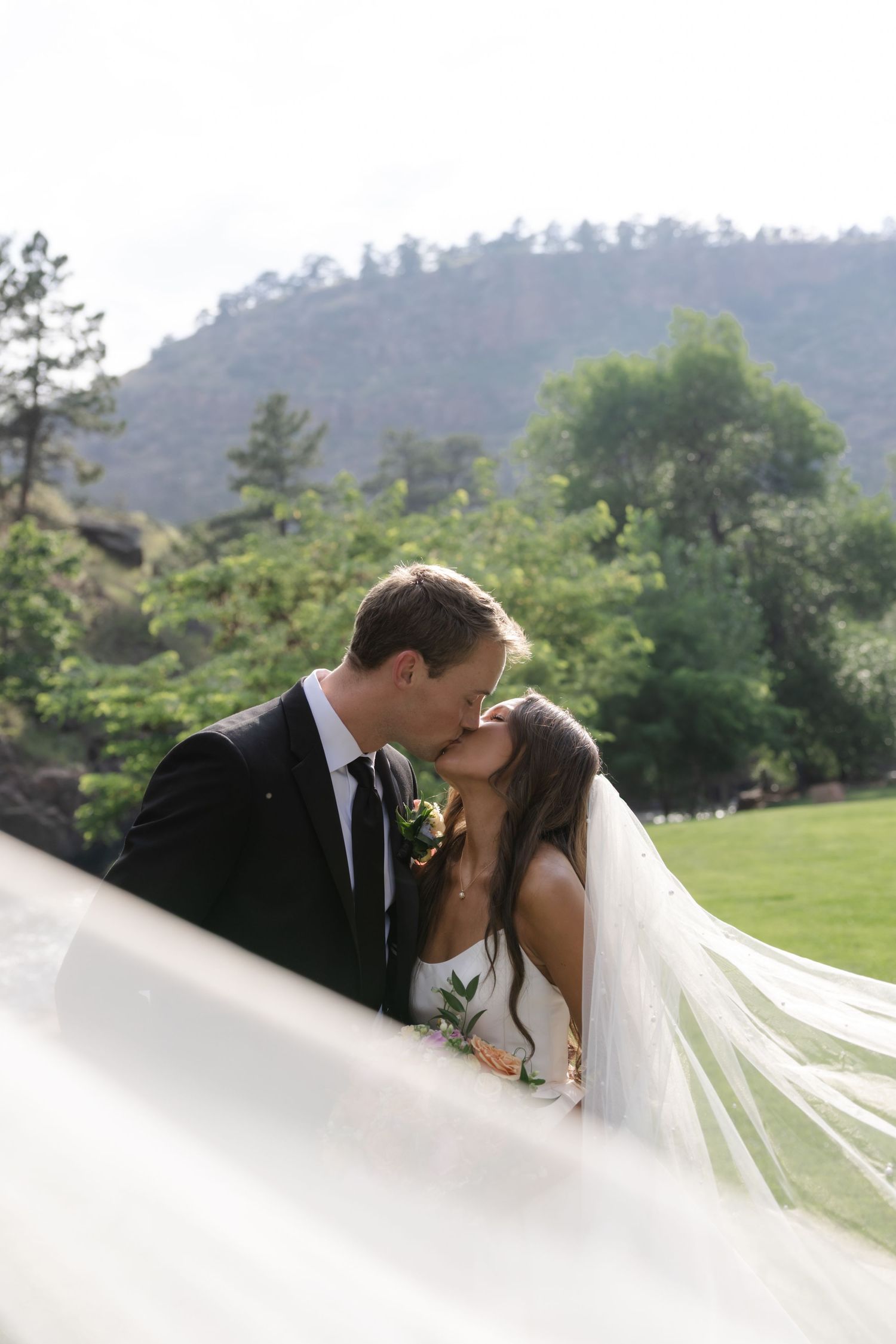 Romantic wedding portrait with flowing veil against mountain landscape.