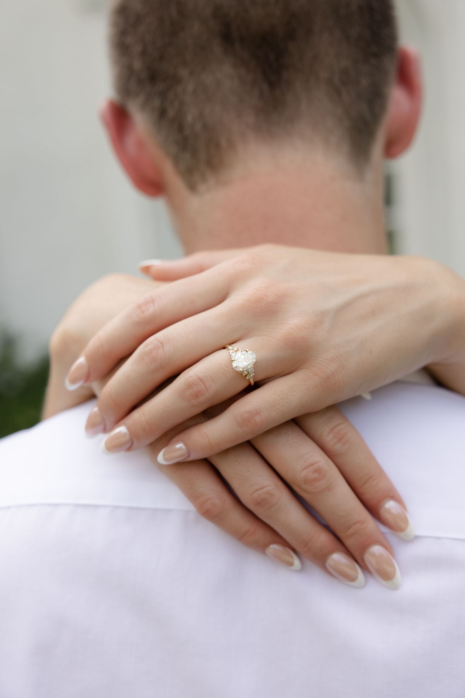 Close-up shot of hands resting on shoulders, showcasing an elegant engagement ring.