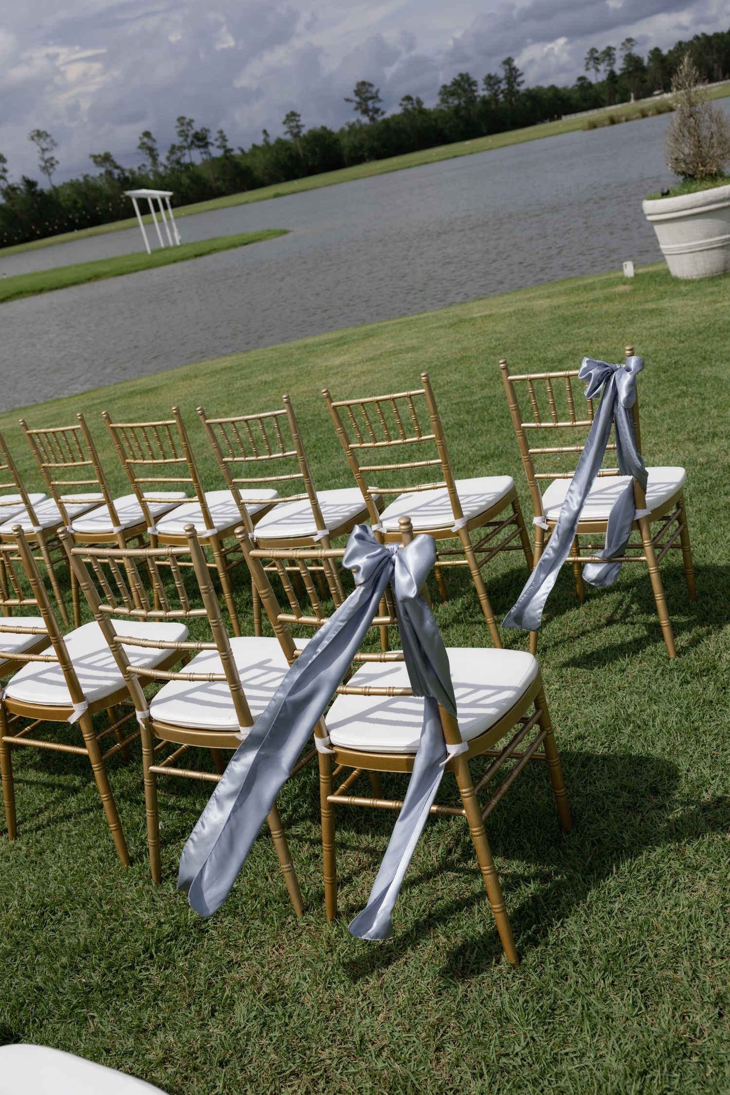 Wooden chiavari chairs with blue sashes arranged outdoors on grass for a wedding ceremony.