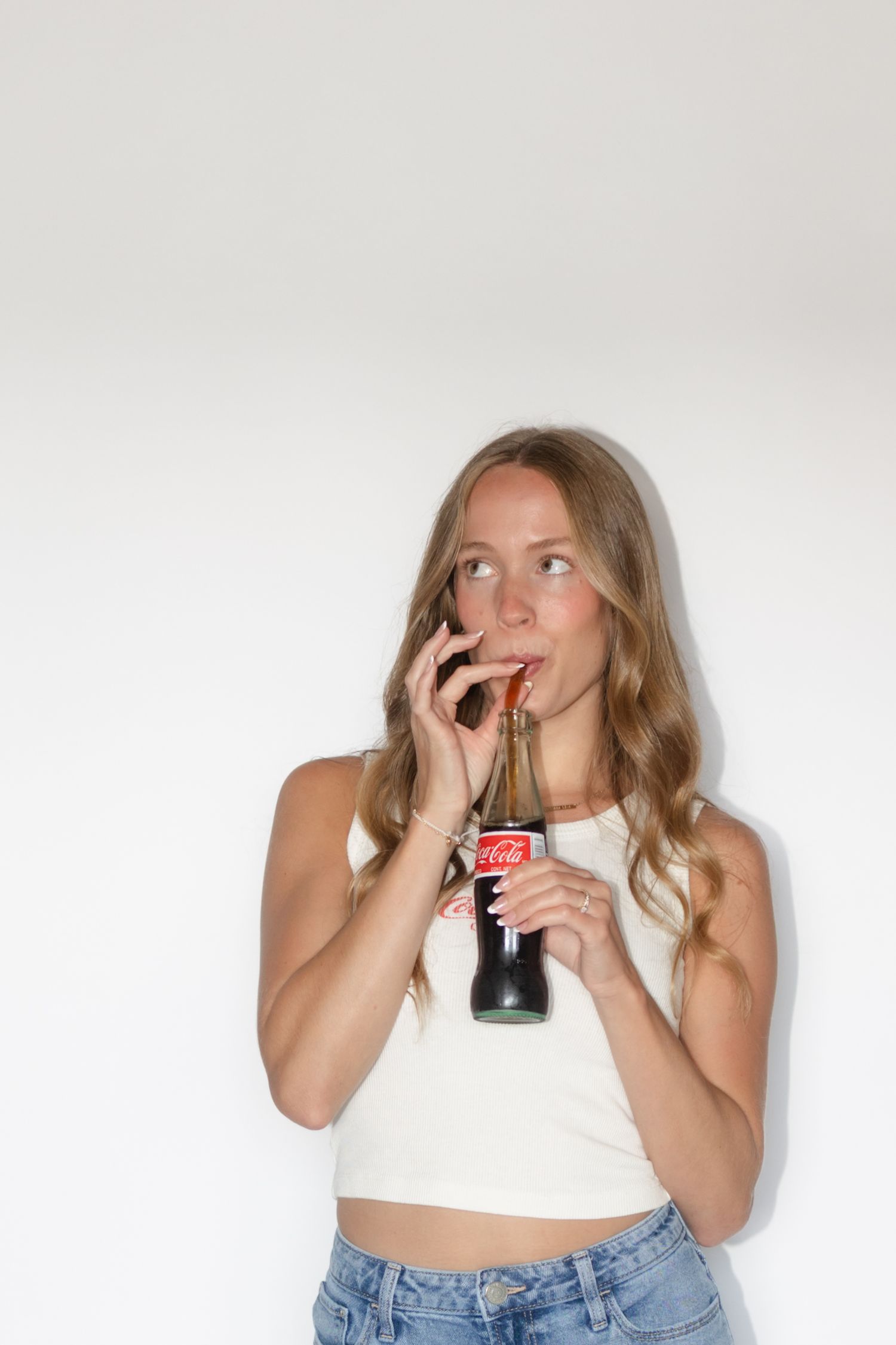 Portrait of person in casual attire drinking from a glass bottle against white background.
