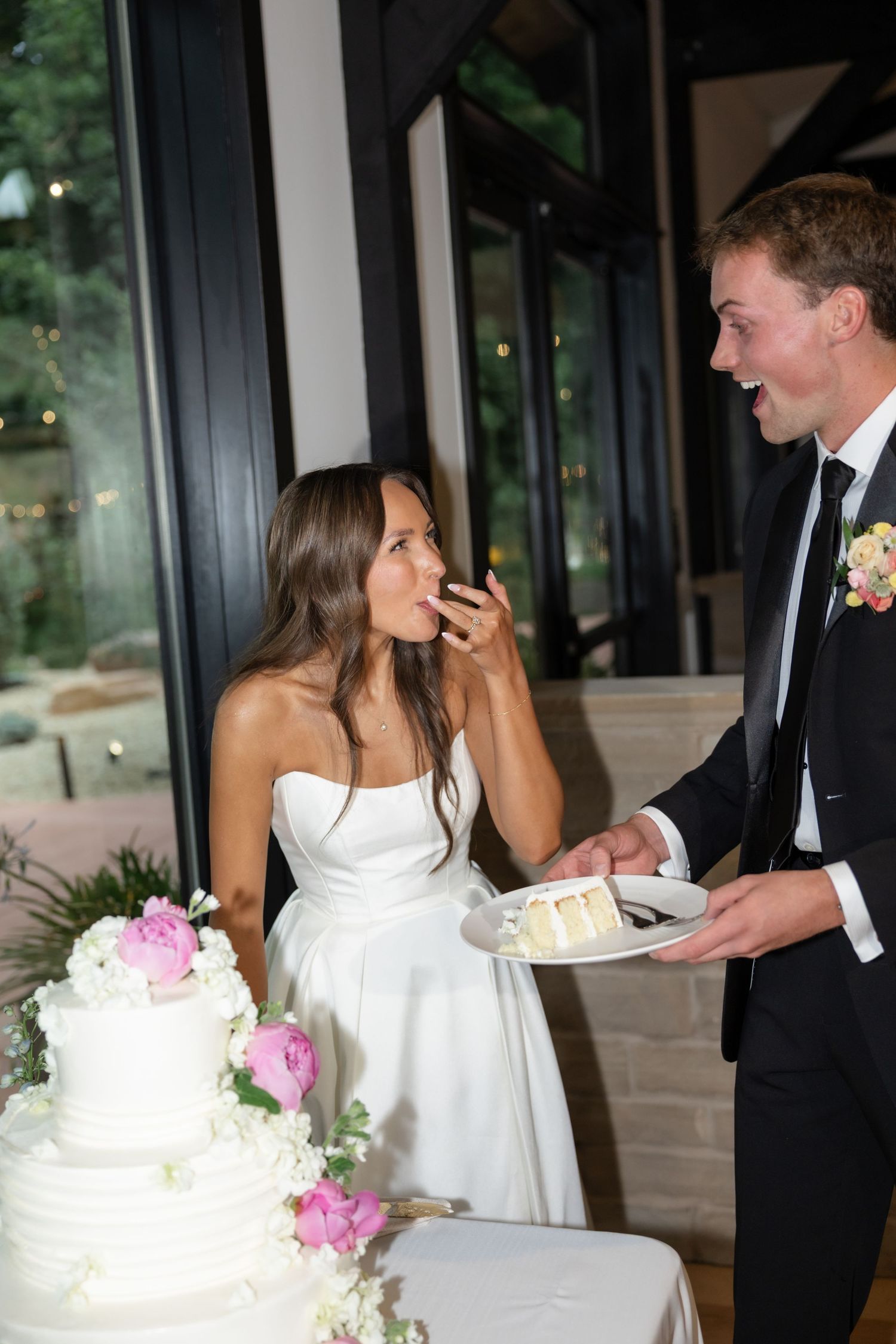 Playful cake feeding moment at wedding reception with elegant white cake.