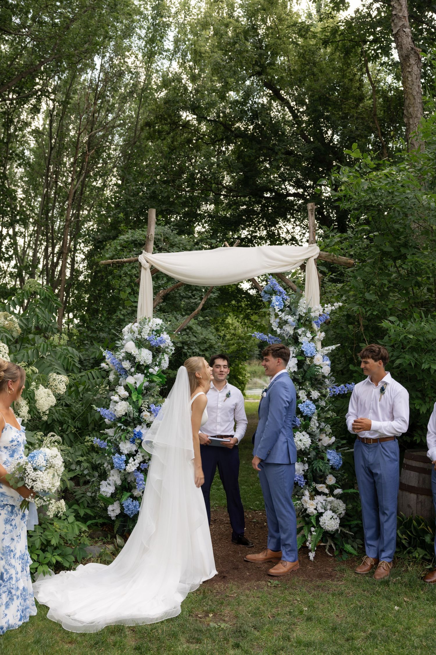 Garden wedding ceremony setup with white fabric arch and blue hydrangea floral arrangements.