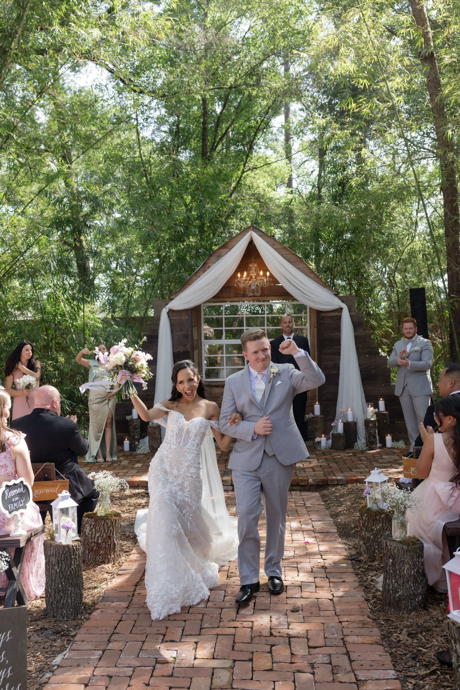 Wedding ceremony site with wooden arch and white draping surrounded by trees.