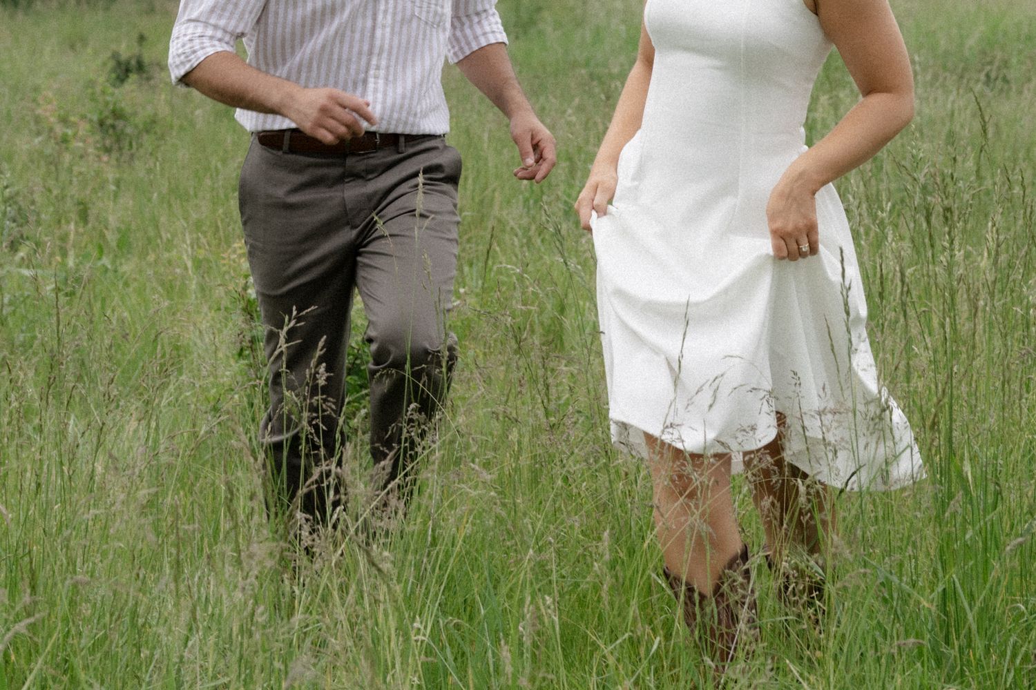 A couple spins and dances through a field of tall grass on a summer day.