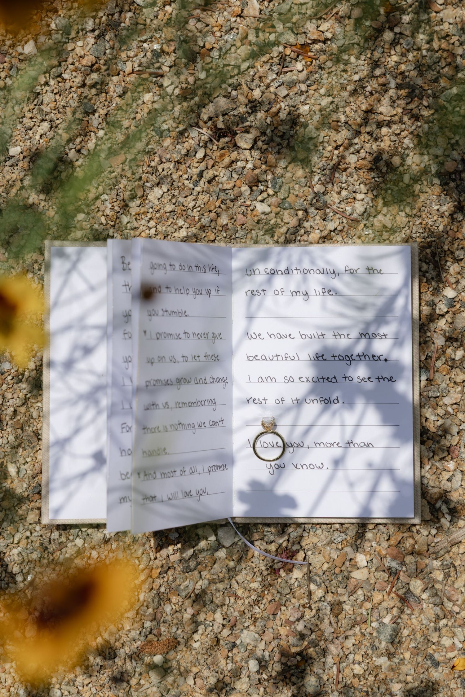 Wedding ring photographed on an open invitation book with handwritten text in natural lighting.