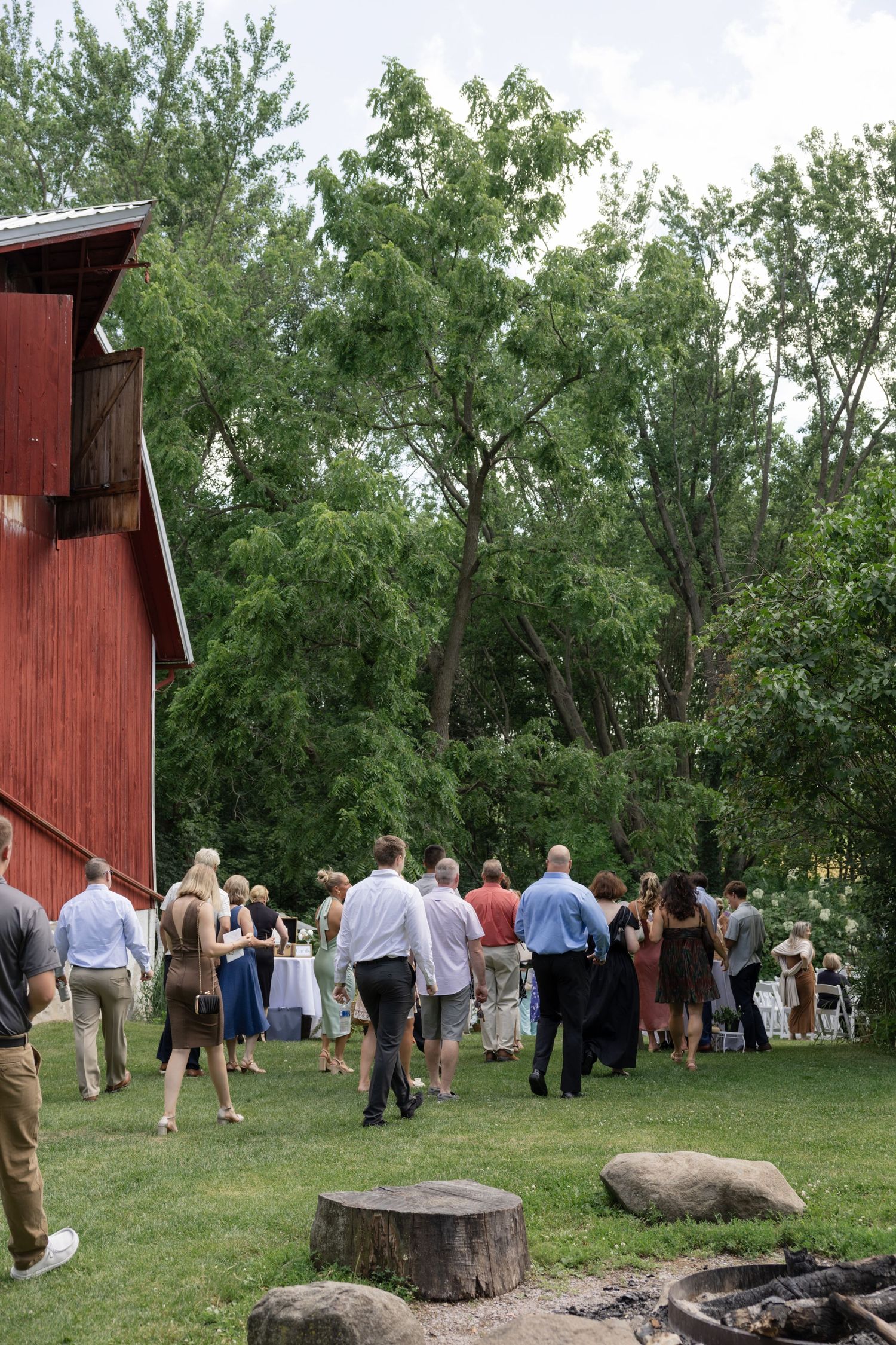 Outdoor wedding ceremony setup with guests gathered near a red barn.
