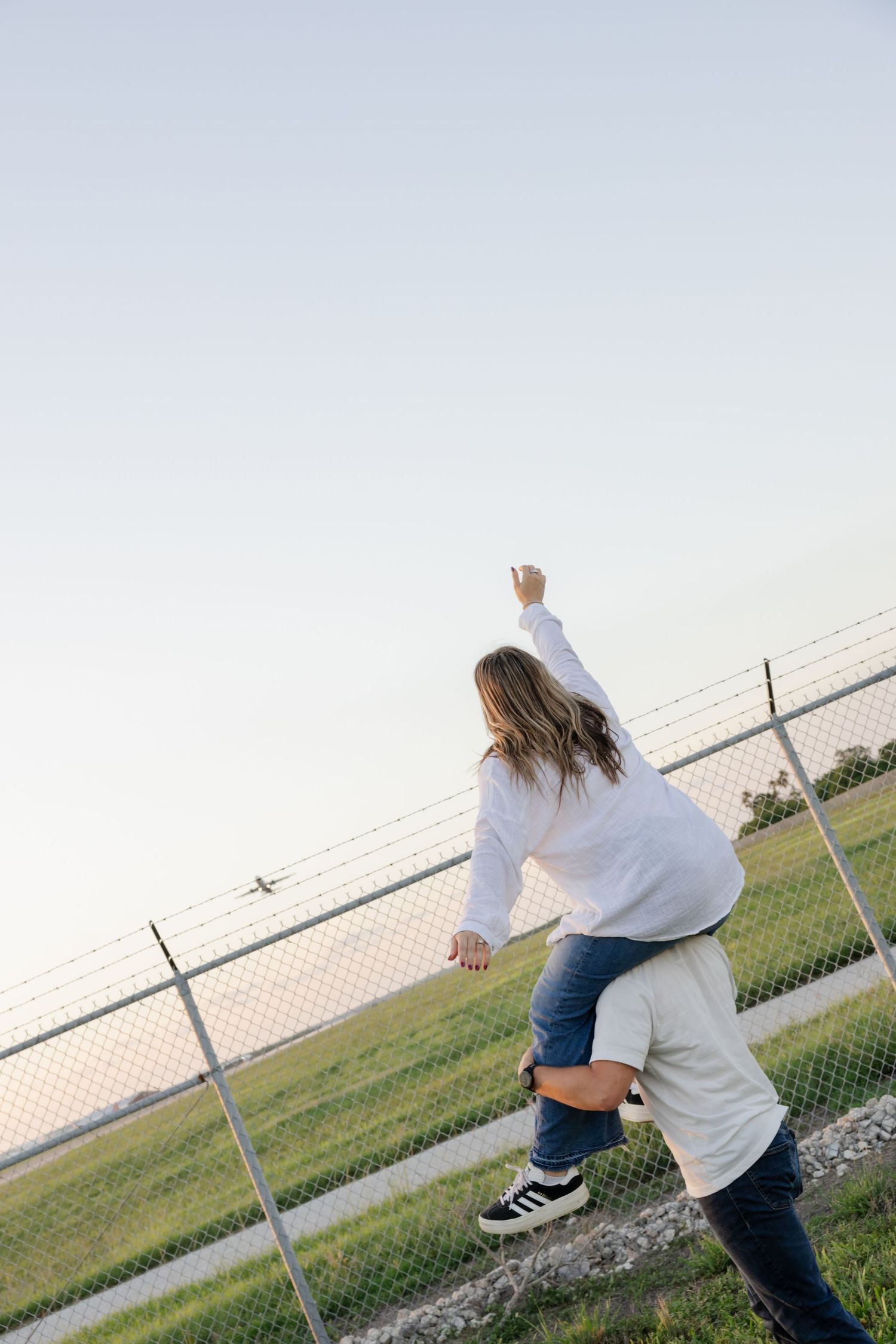 People excitedly waving at passing aircraft from behind airport security fence.