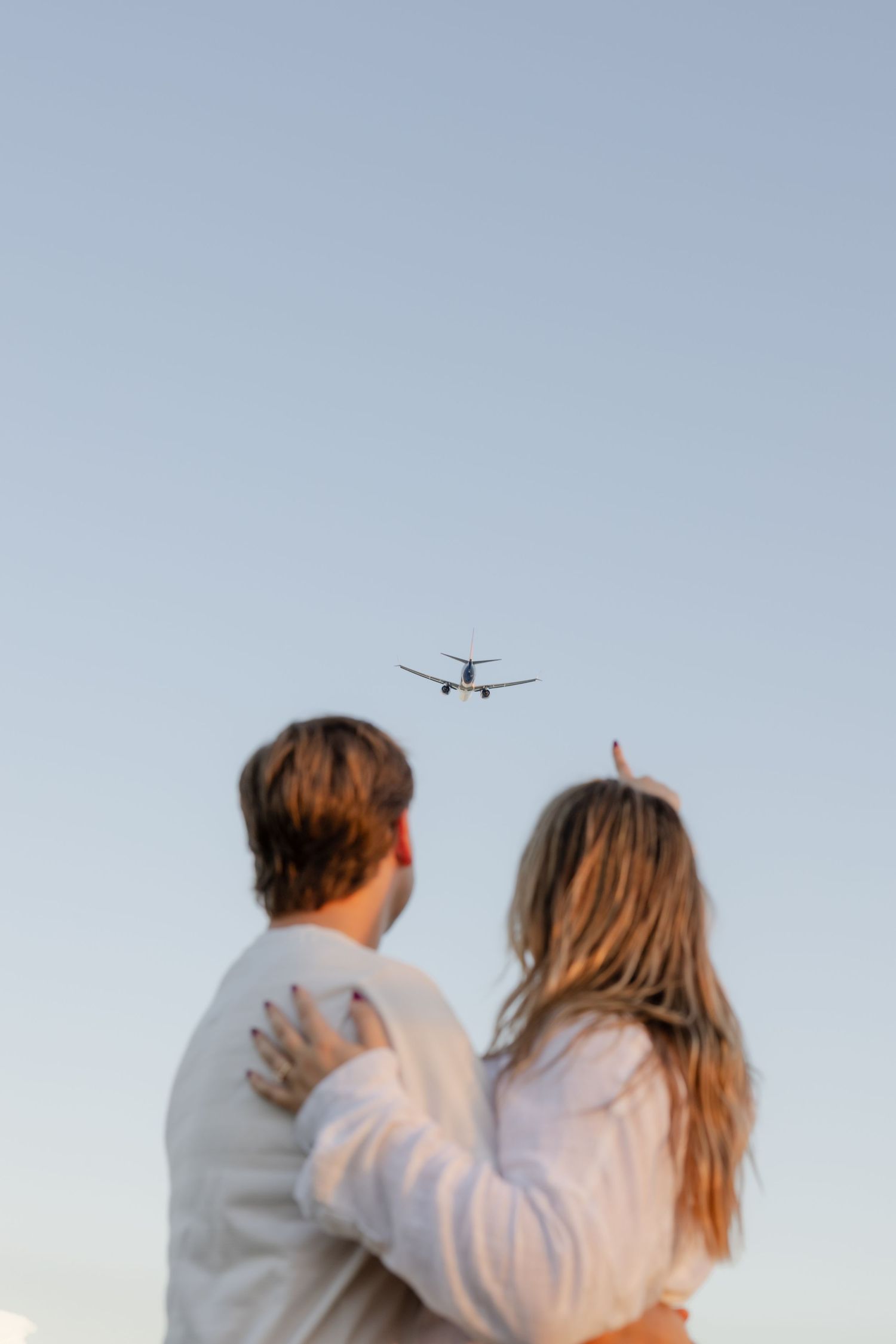 Two people embracing while watching planes fly overhead at sunset.