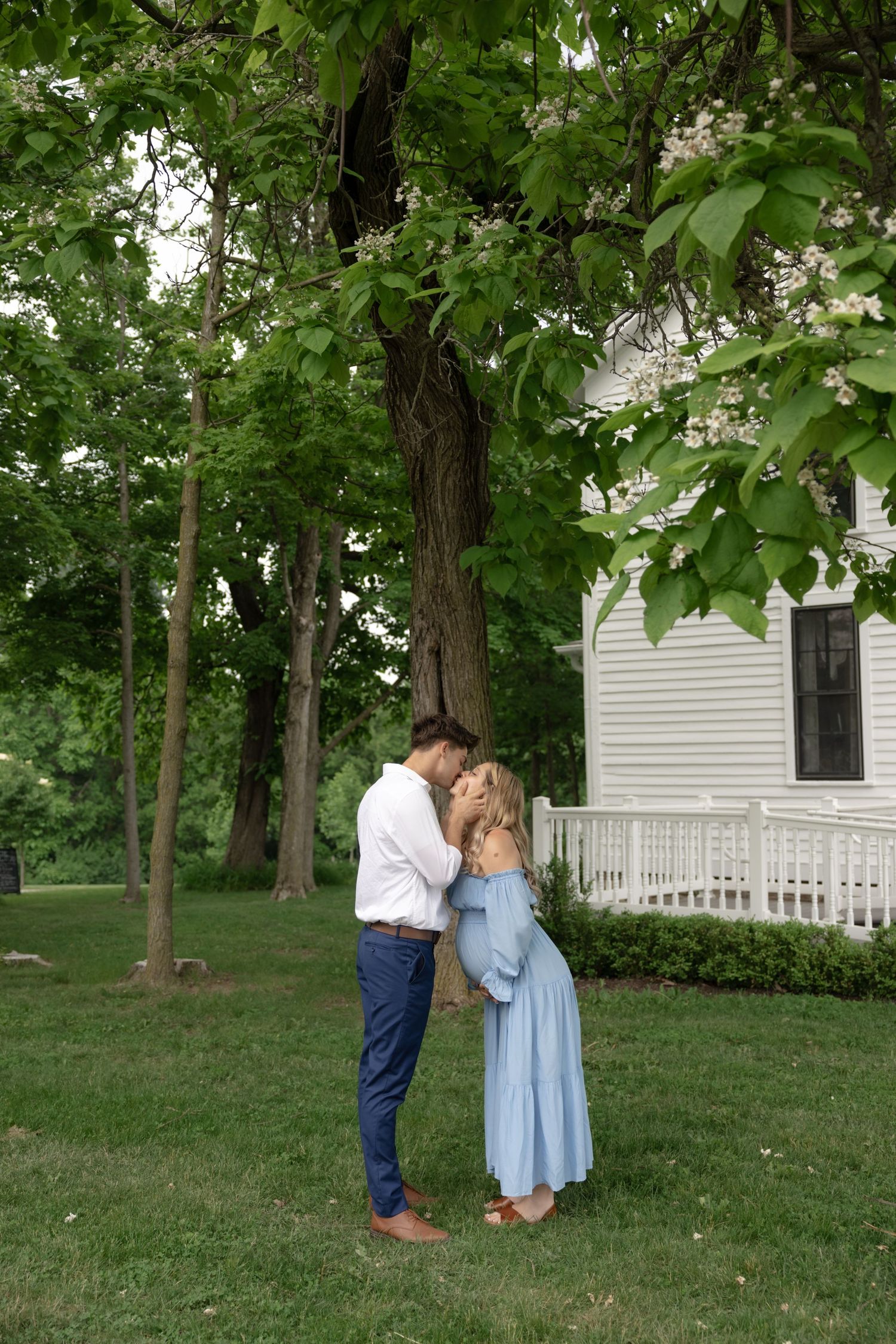 Couple sharing an intimate moment on a lawn in front of a white house.