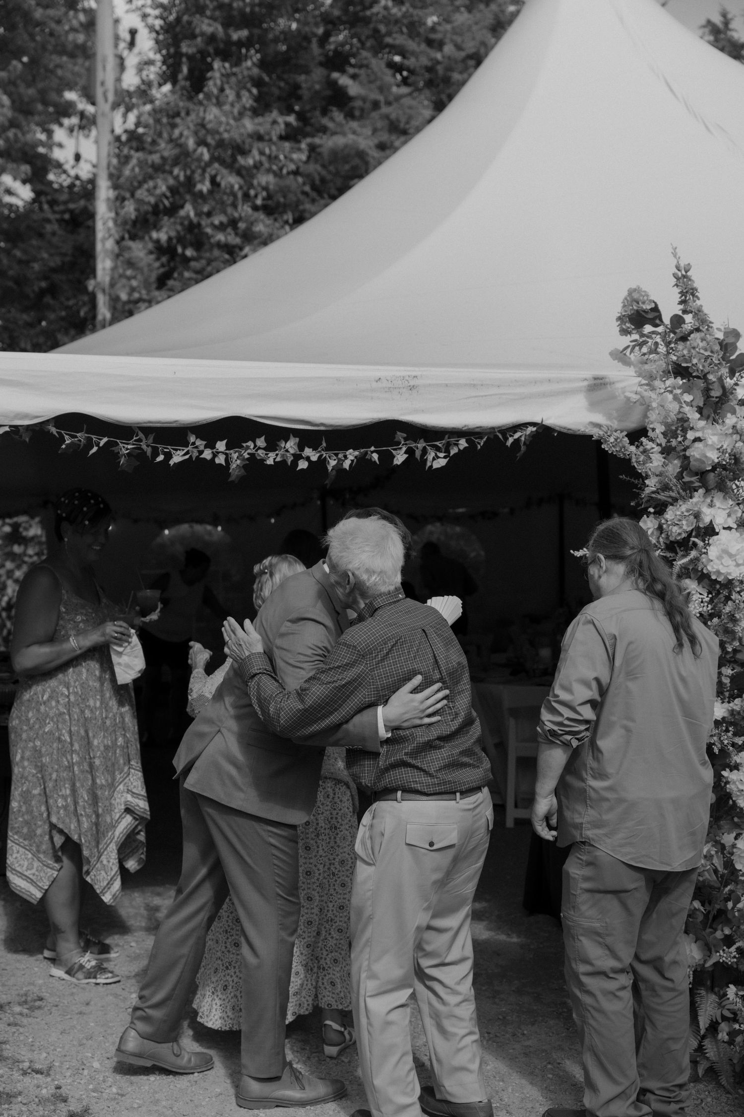 Wedding guests dancing under a white tent canopy at an outdoor reception.