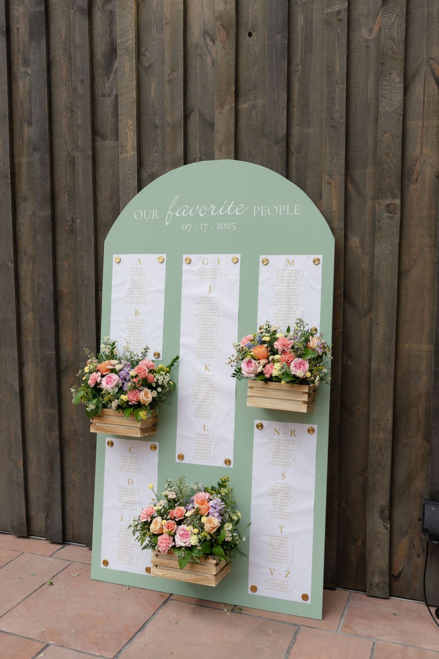 Mint green wedding seating chart display decorated with floral boxes against wooden fence.