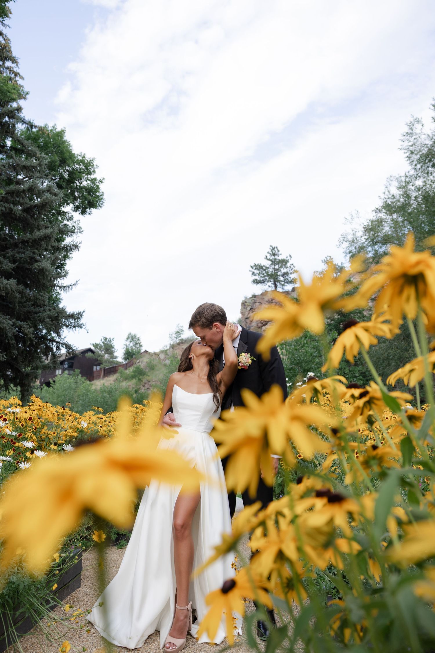 A romantic embrace among yellow wildflowers with mountain cliffs in the background.
