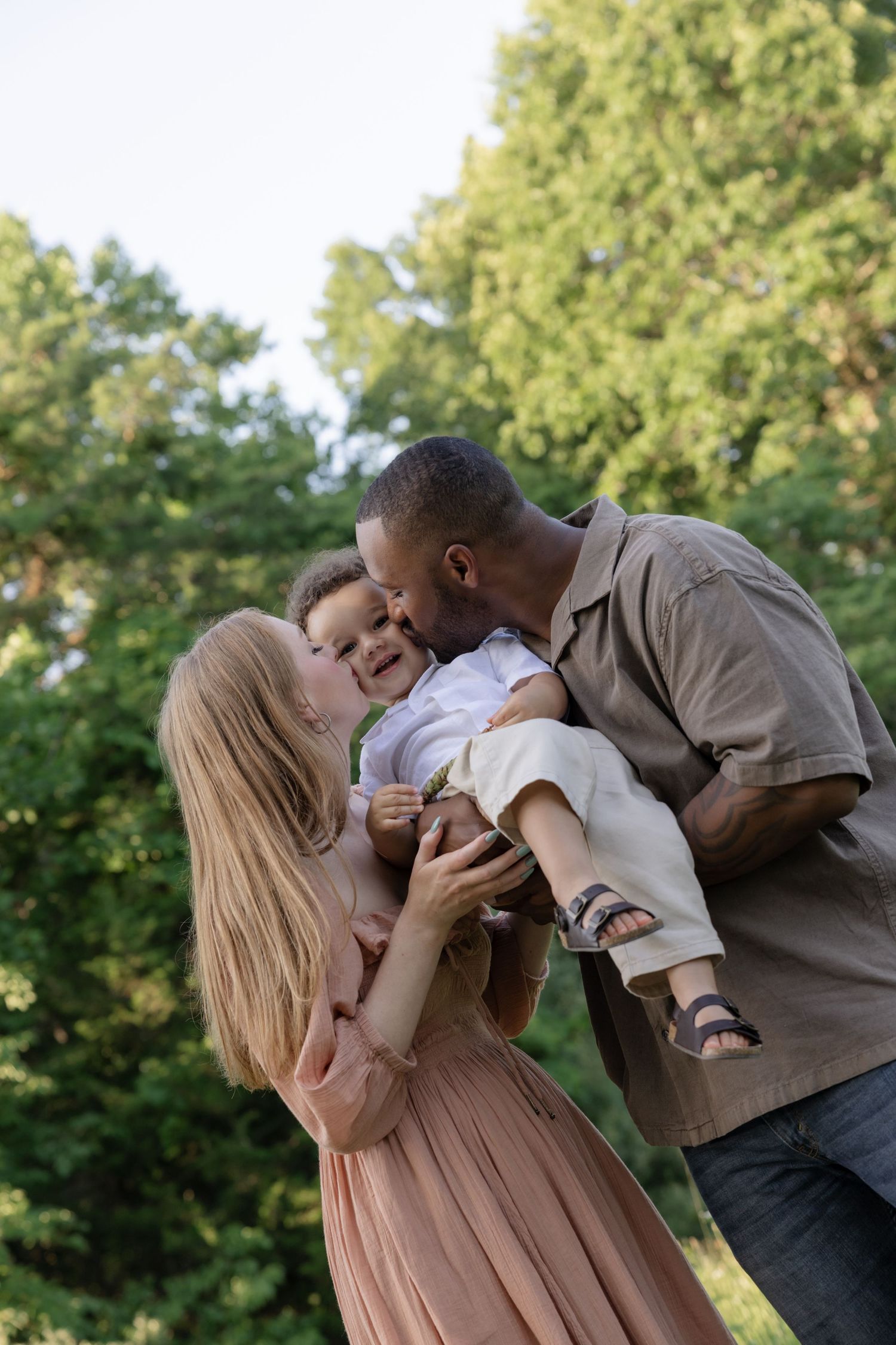 A family sharing tender moments with their baby in a sunny outdoor setting.