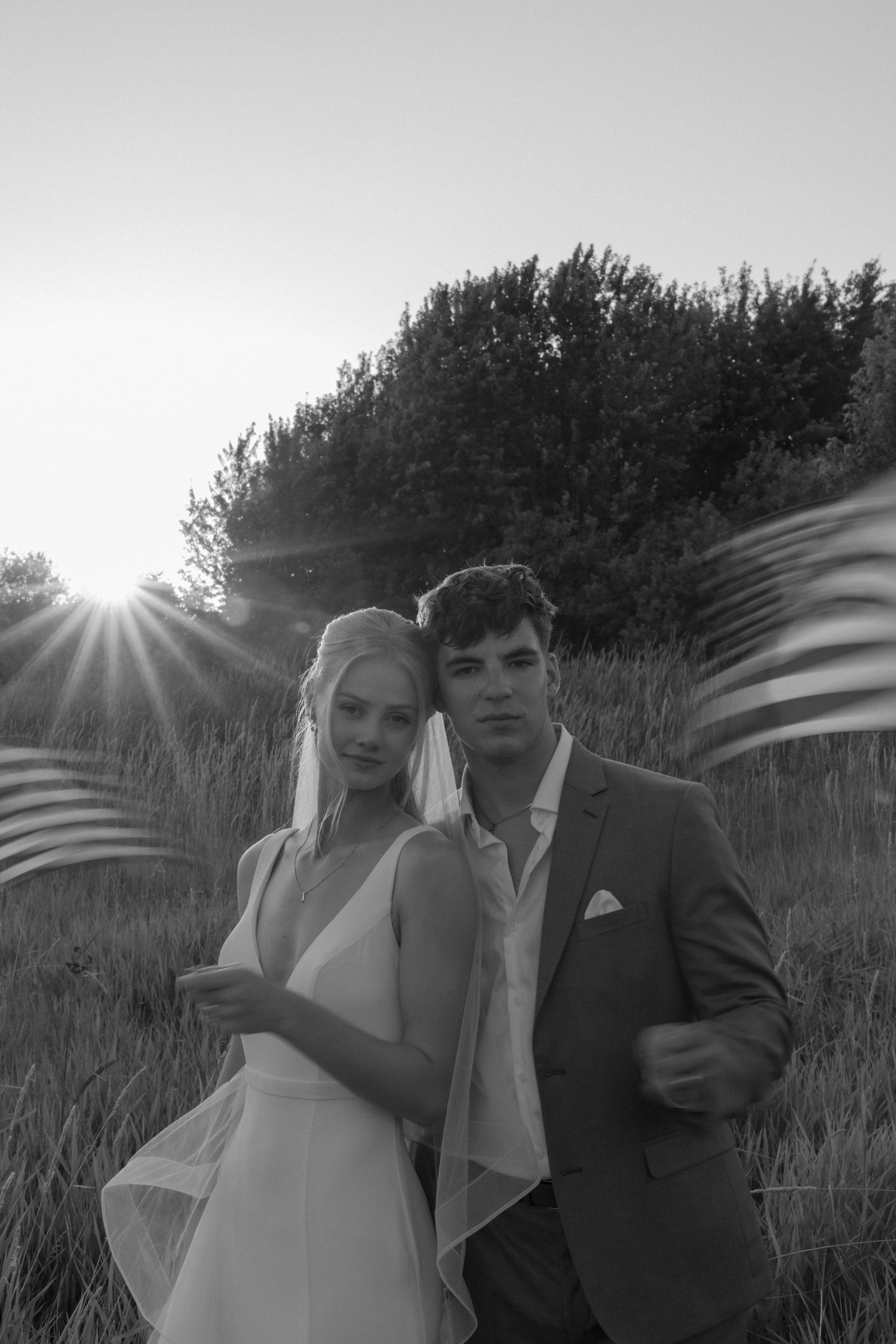 Black and white photo series of a couple with flowing veil at sunset in a natural setting.