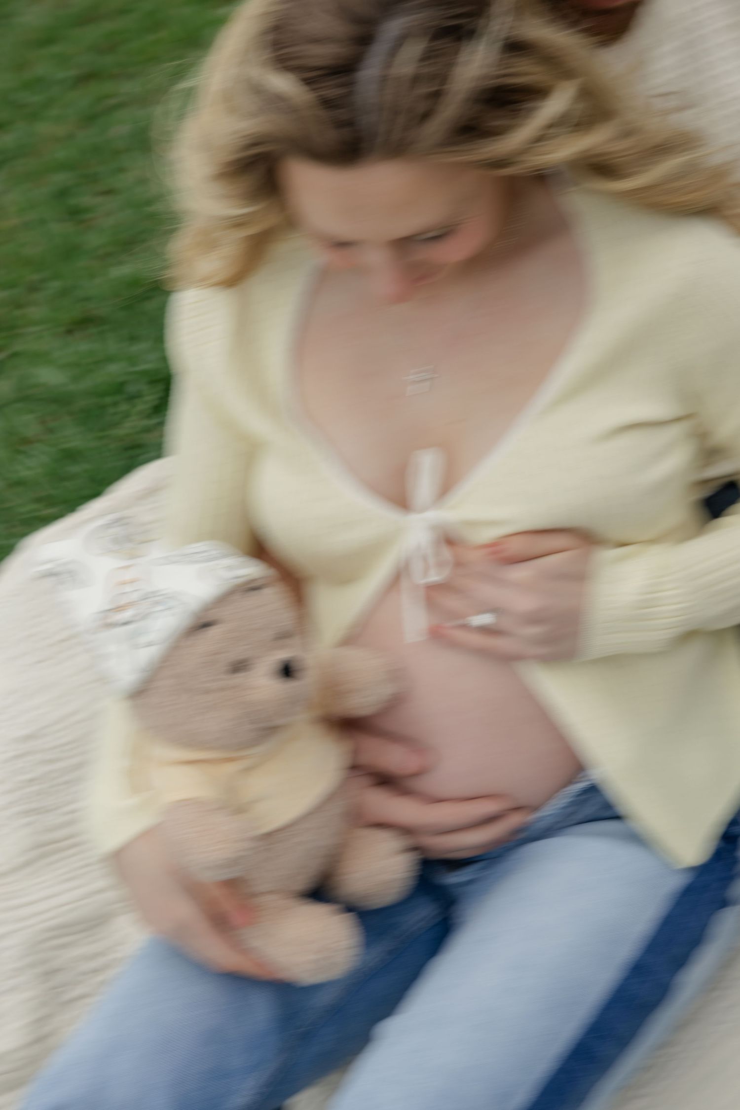 Artistic blurred shot of pregnant belly with teddy bear and cream cardigan.