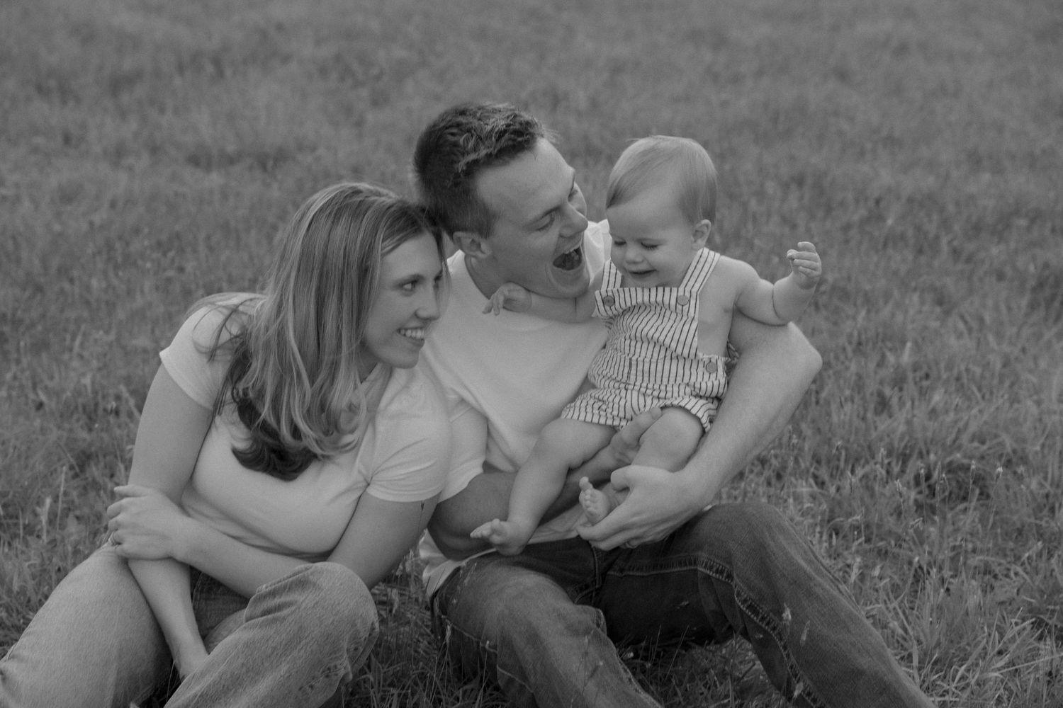 A family of three relaxes together on grass in black and white.