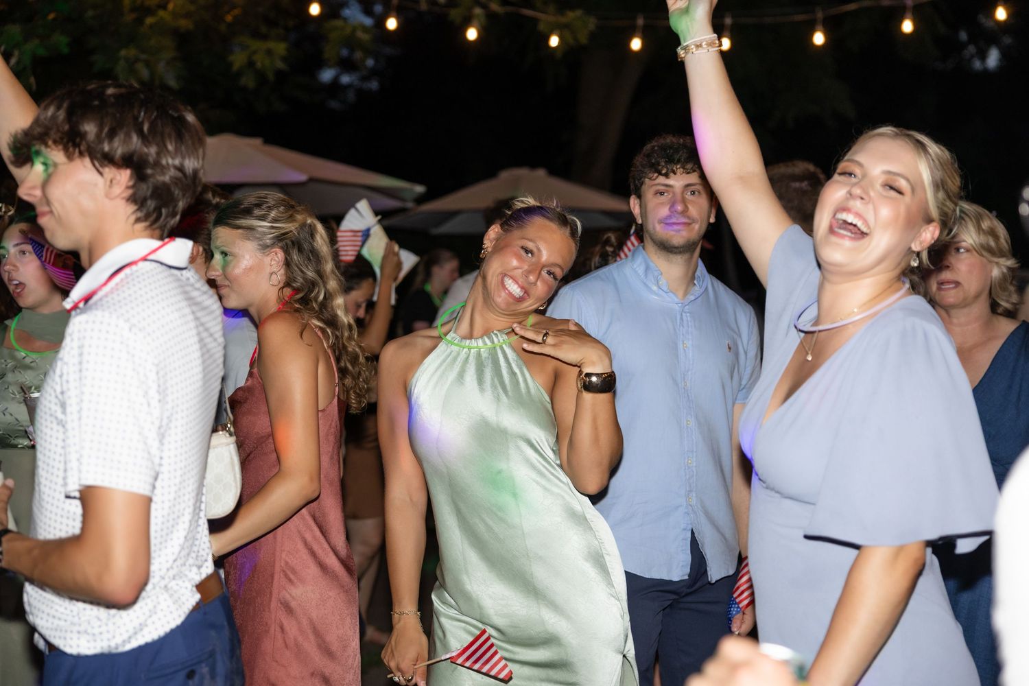 Energetic party crowd dancing under string lights outdoors.