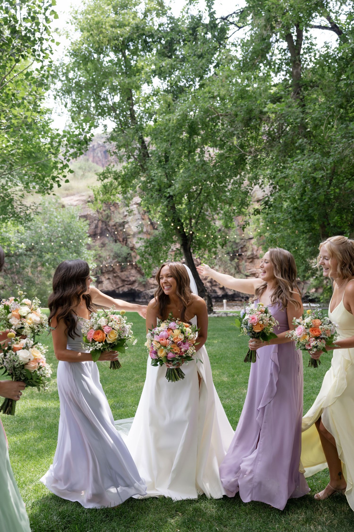 Bridesmaids in lavender and white dresses having fun with floral bouquets outdoors.