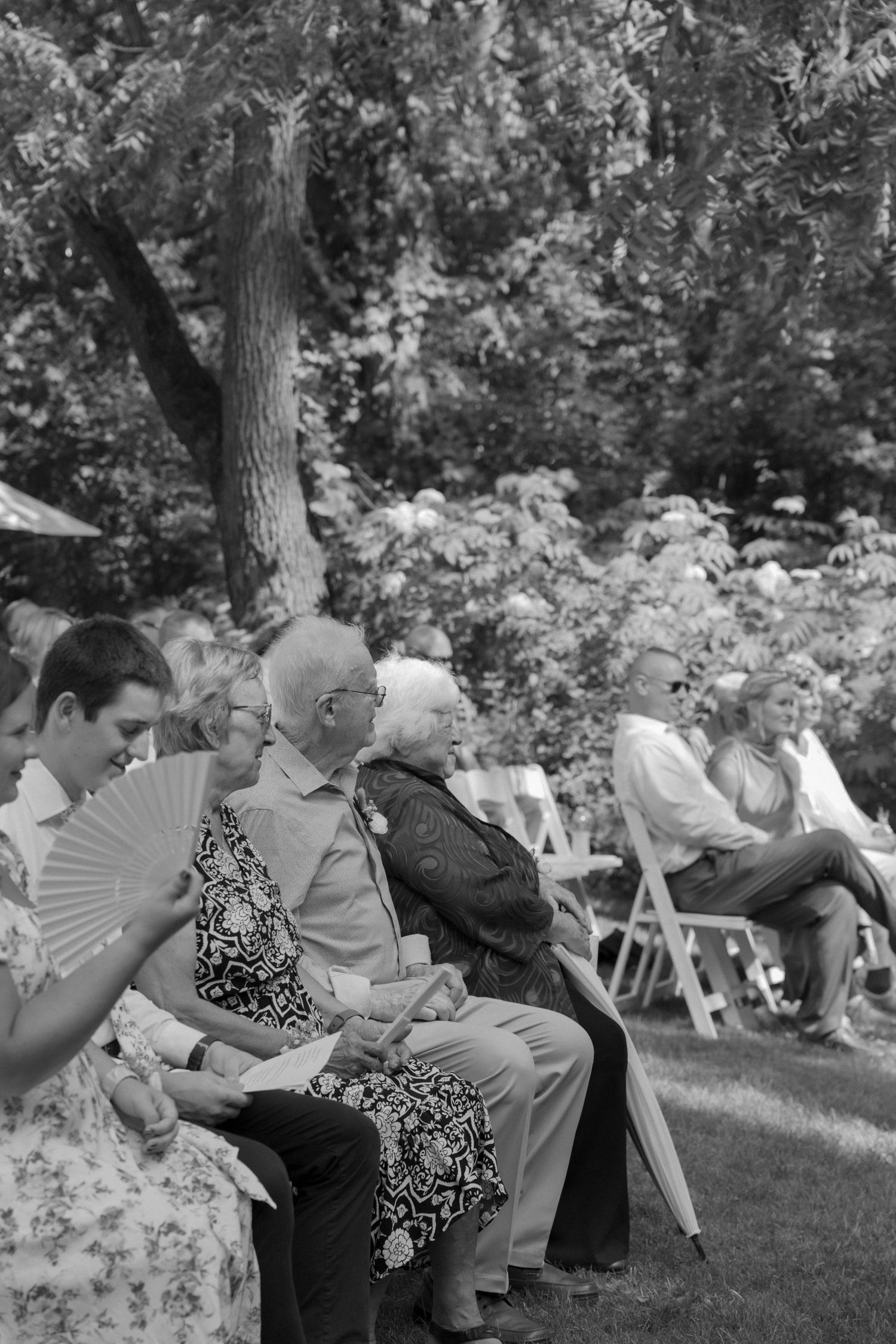 Black and white photo of guests seated in rows at an outdoor garden gathering.