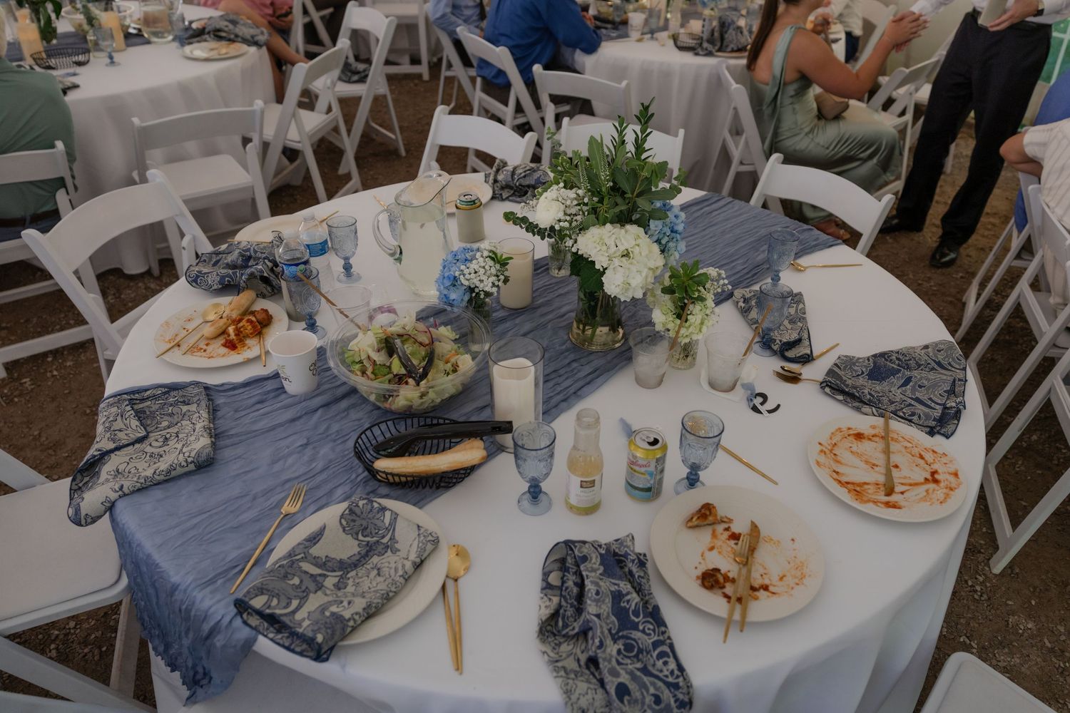 Place settings and table decorations at an outdoor wedding reception with white linens.
