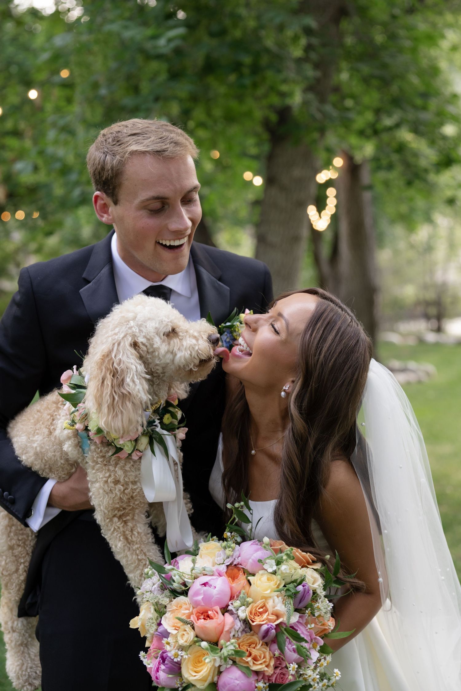 Couple shares joyful moment with fluffy white dog during outdoor wedding photoshoot.