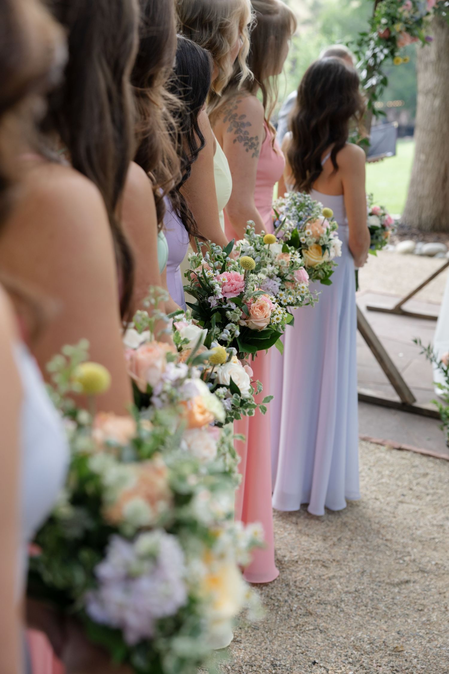 Bridesmaids in pastel dresses holding delicate floral bouquets of pink and white flowers.