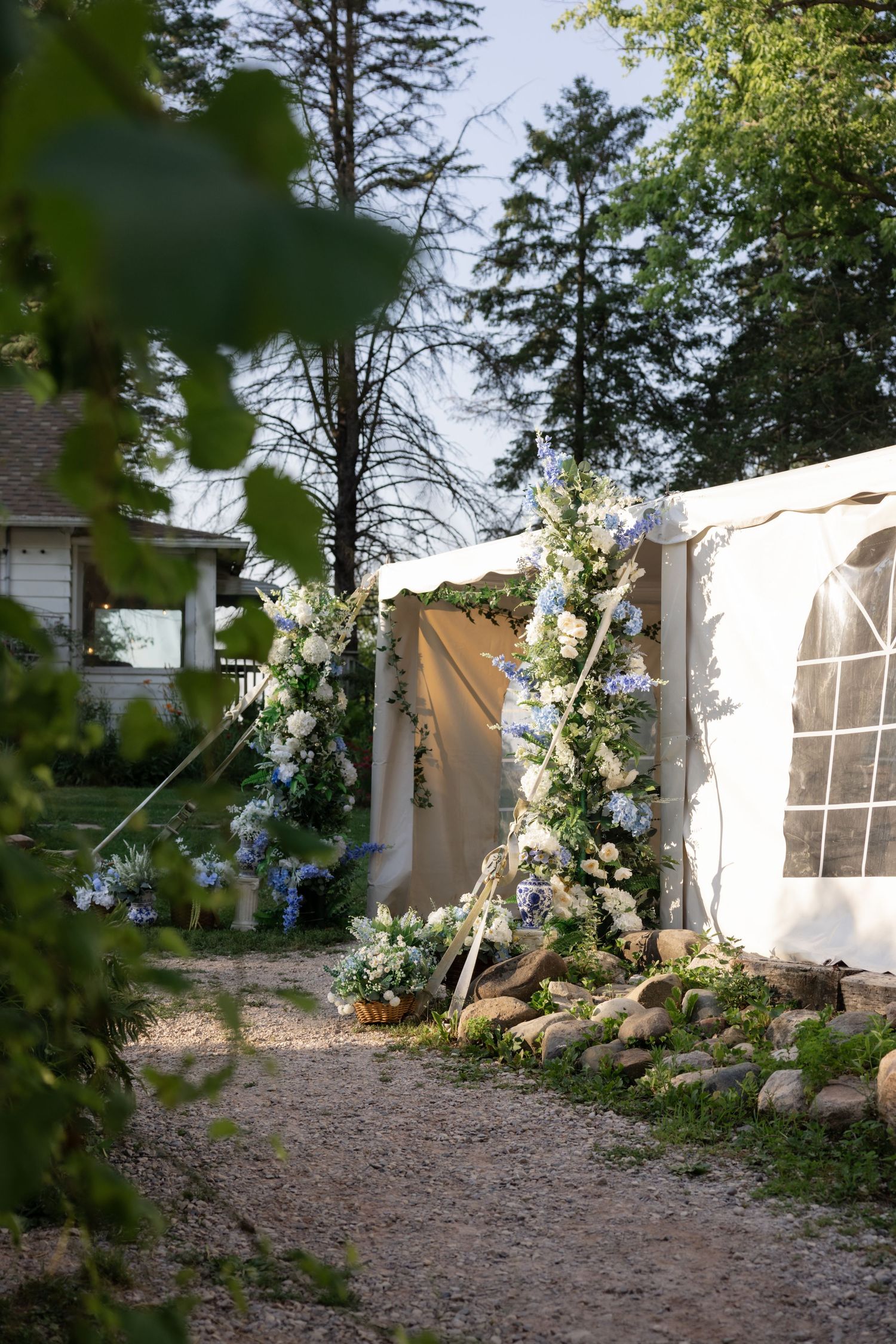 White floral arrangements decorate the entrance to a wedding tent in a garden setting.