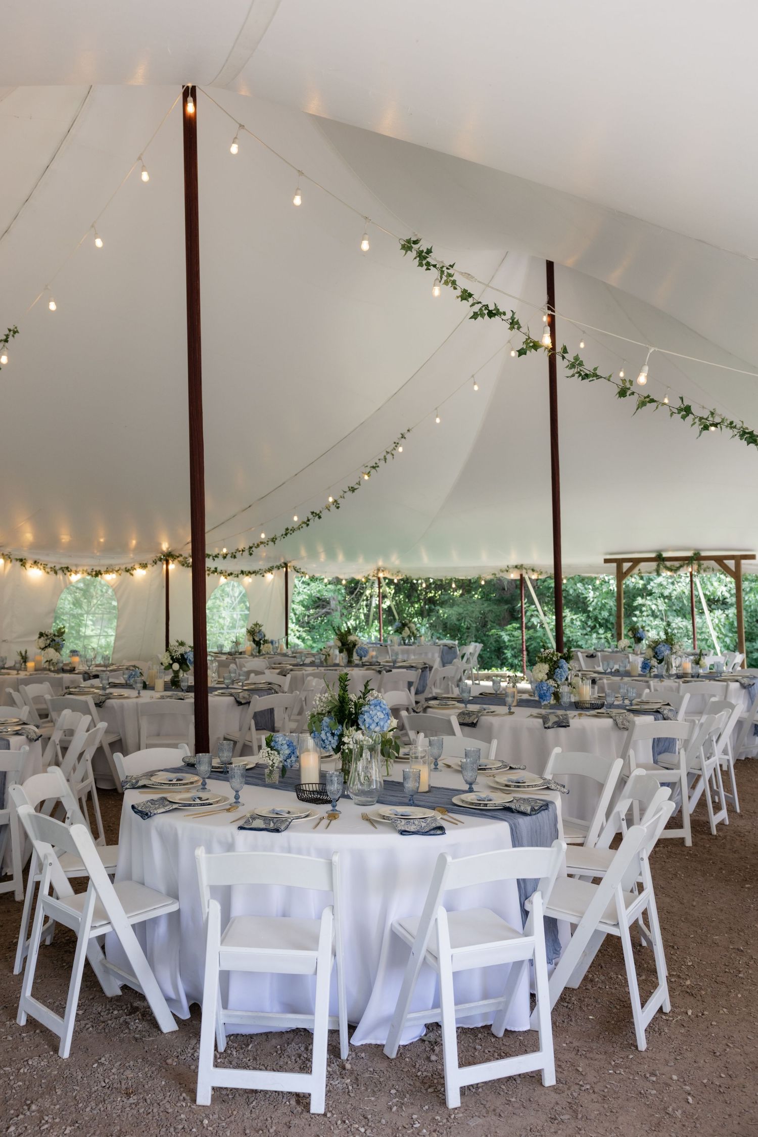 Wedding reception tent decorated with string lights and white tables and chairs.