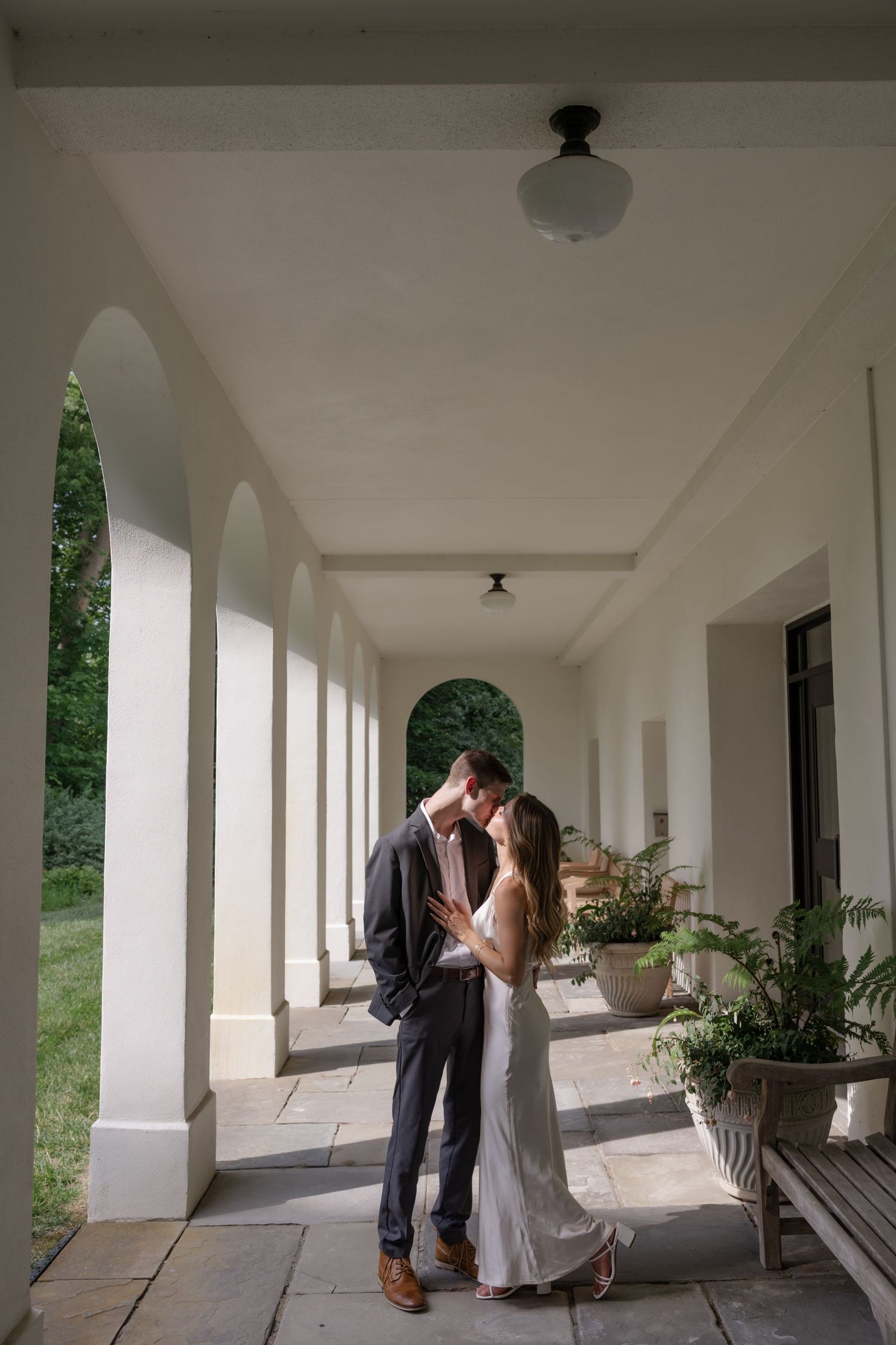 Romantic scene under white colonnade with potted plants and garden views.