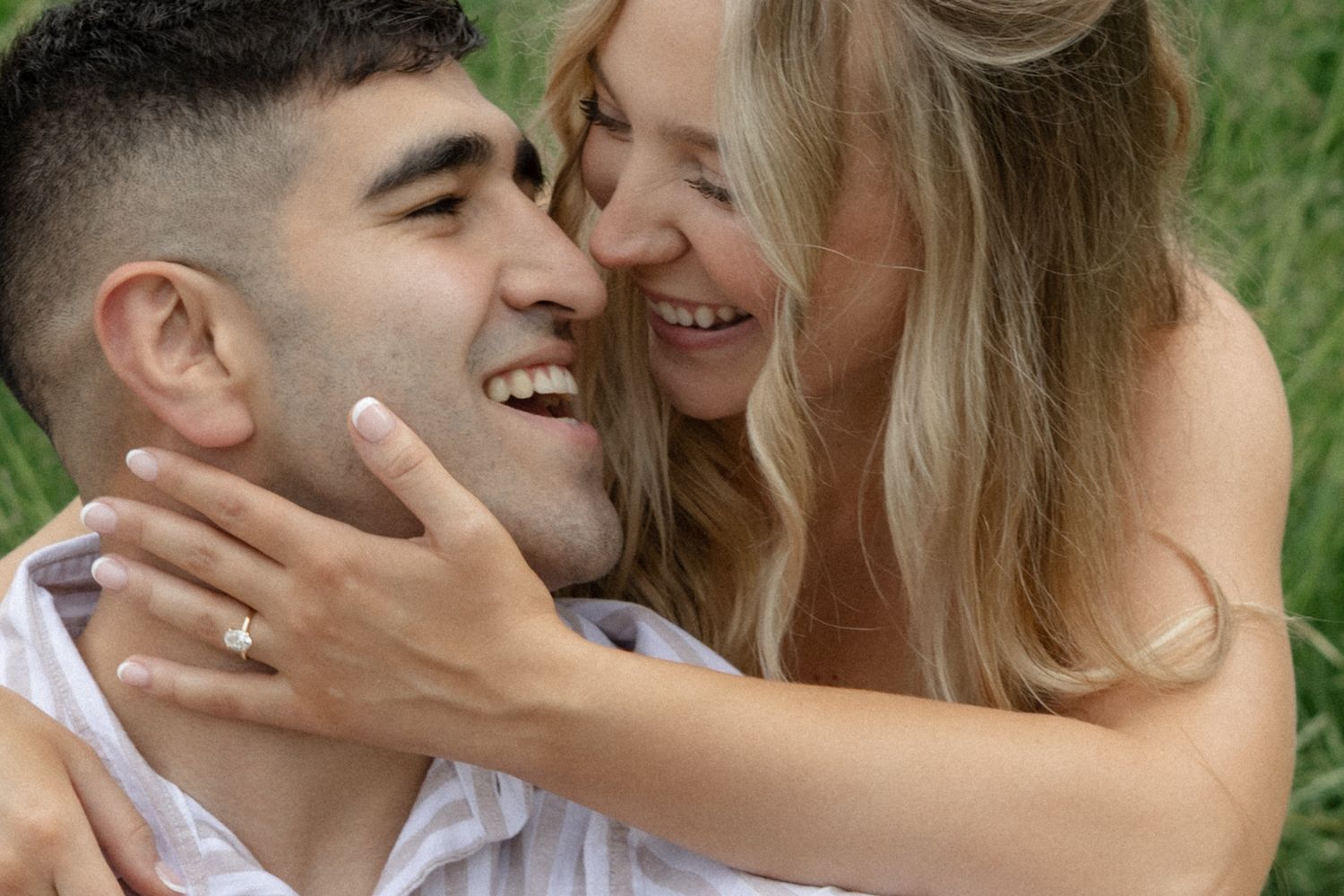 A couple shares joyful laughter while embracing outdoors in natural lighting.