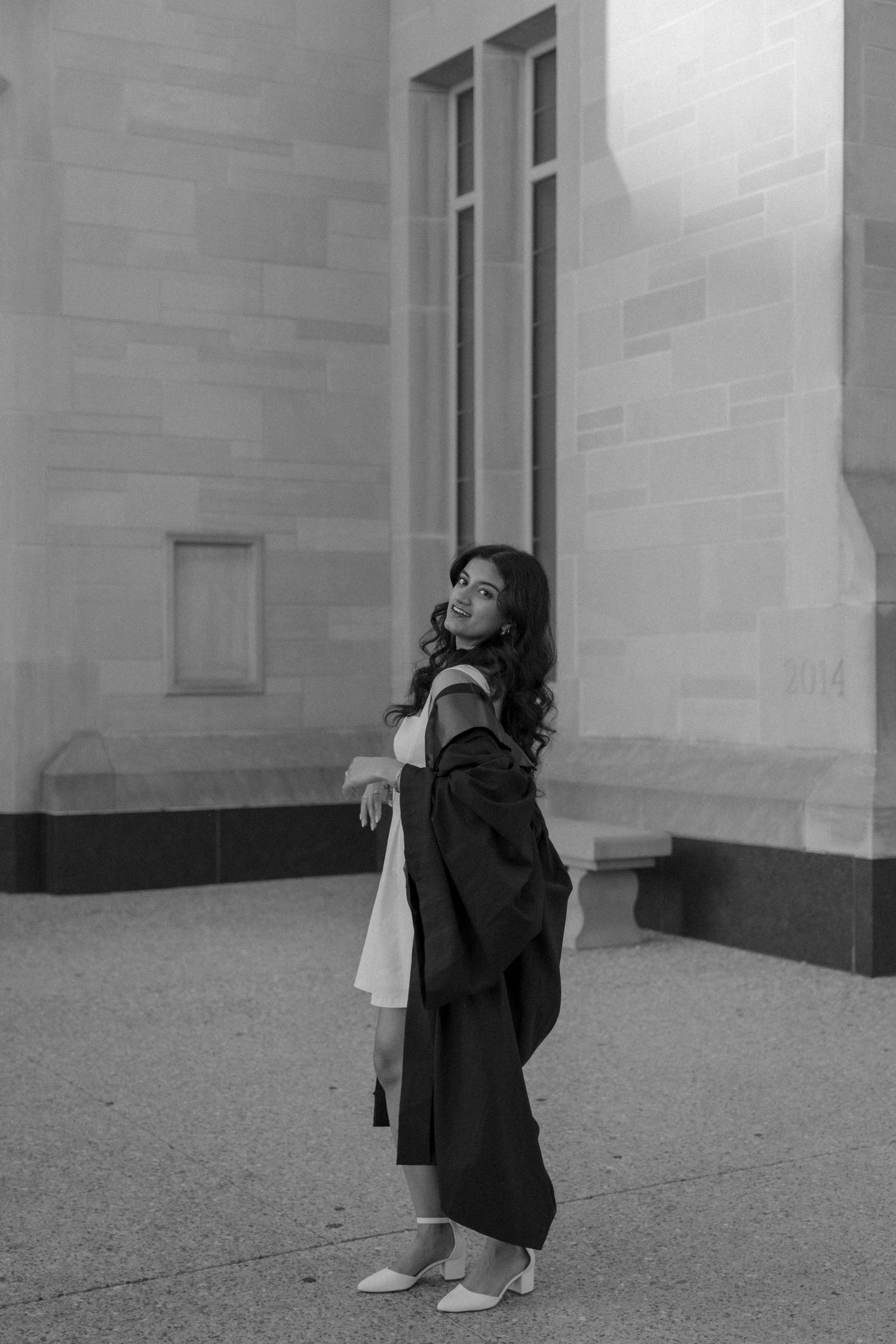 Black and white photo showing a figure posing against stone walls in an architectural setting.