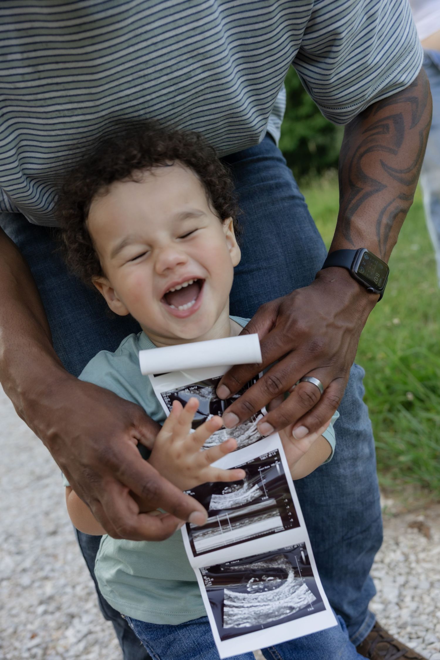 Child laughing while holding ultrasound photos outdoors.
