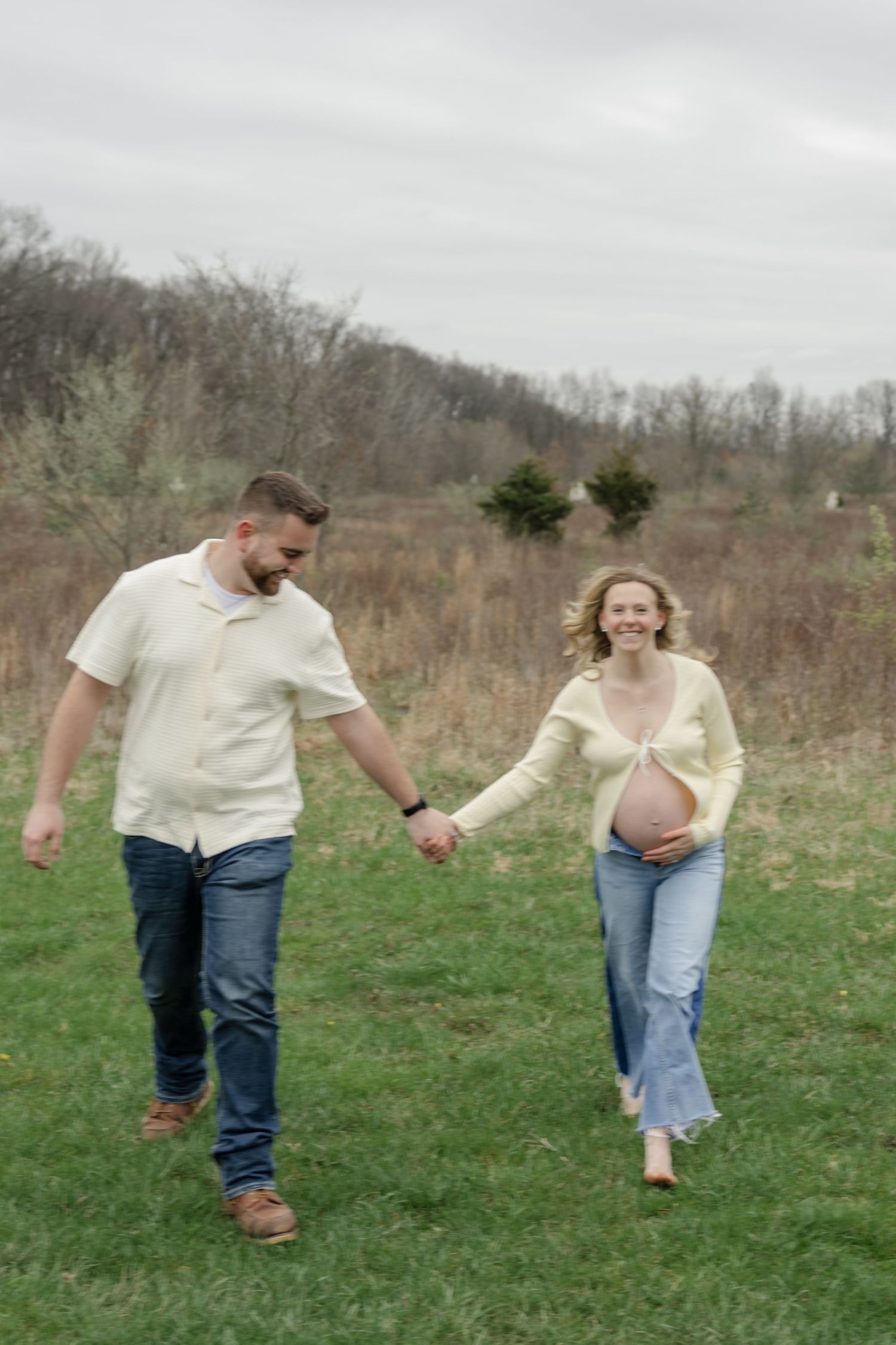 Candid shot of couple holding hands while walking in field during maternity session.