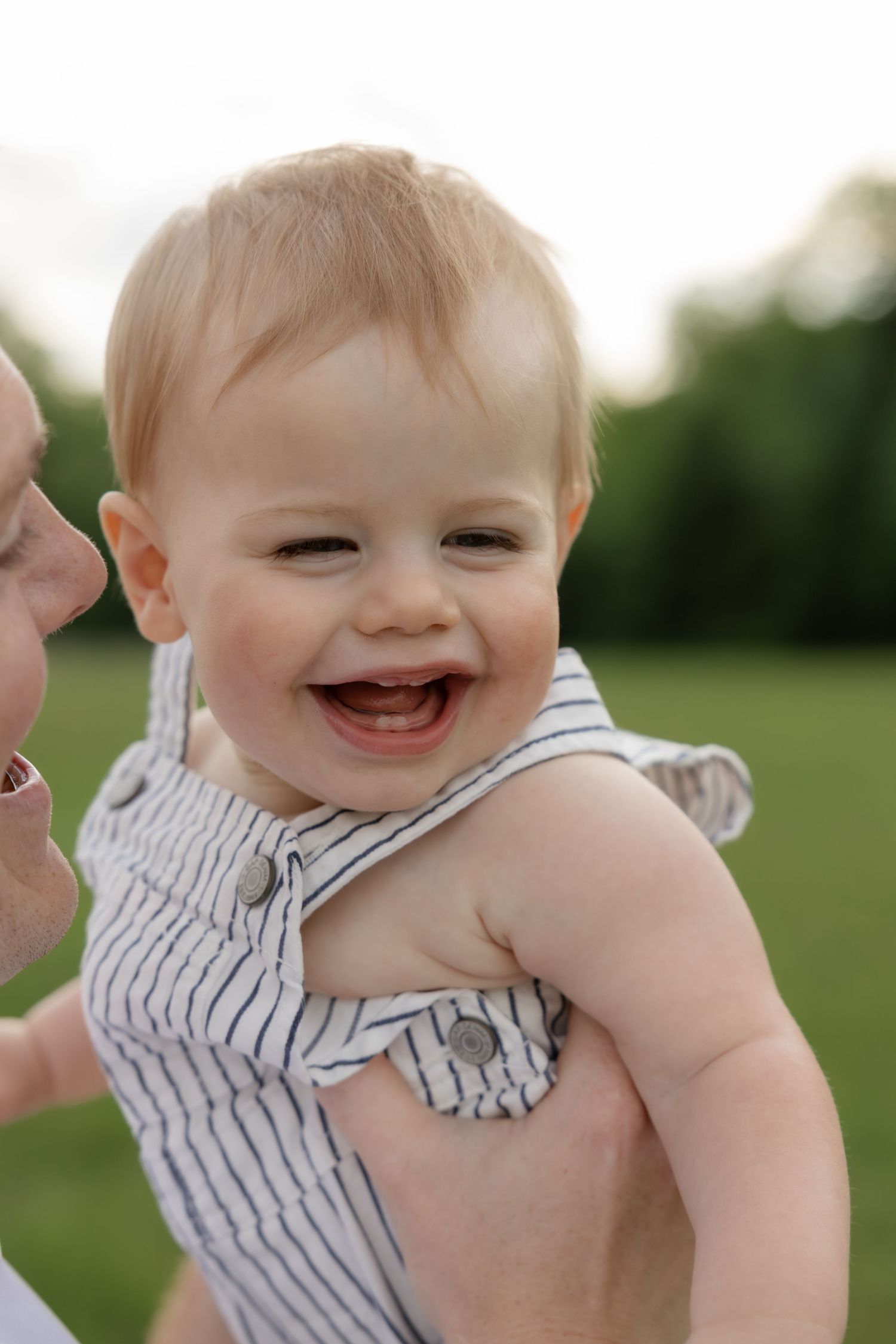 Close-up of a laughing baby wearing a striped outfit outdoors.