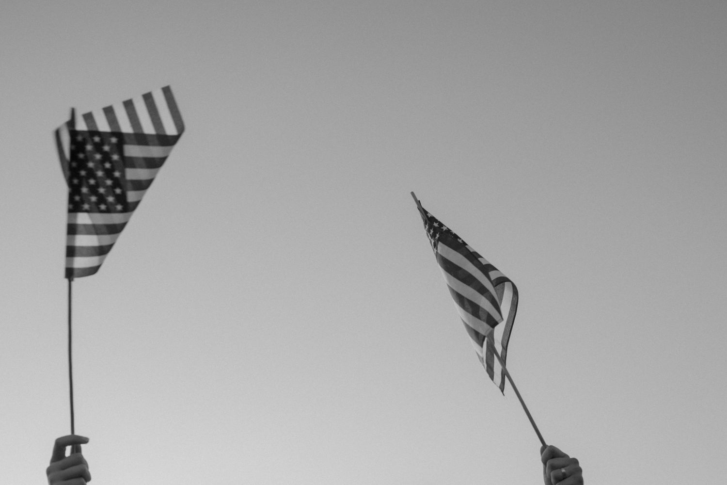 American flags wave against a cloudy gray sky during an outdoor event.