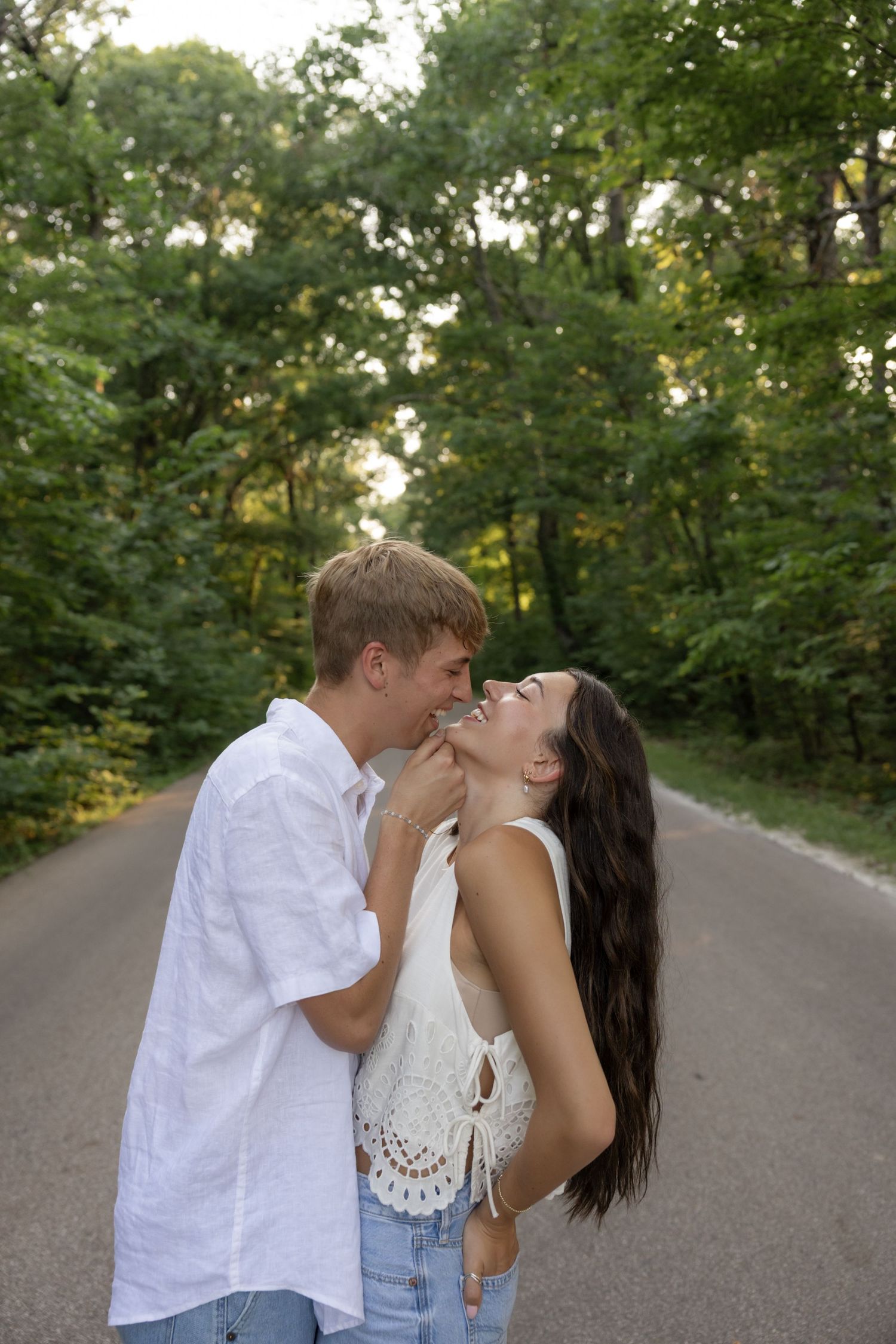 A playful couple shares a laugh together on a tree-lined path in summer.