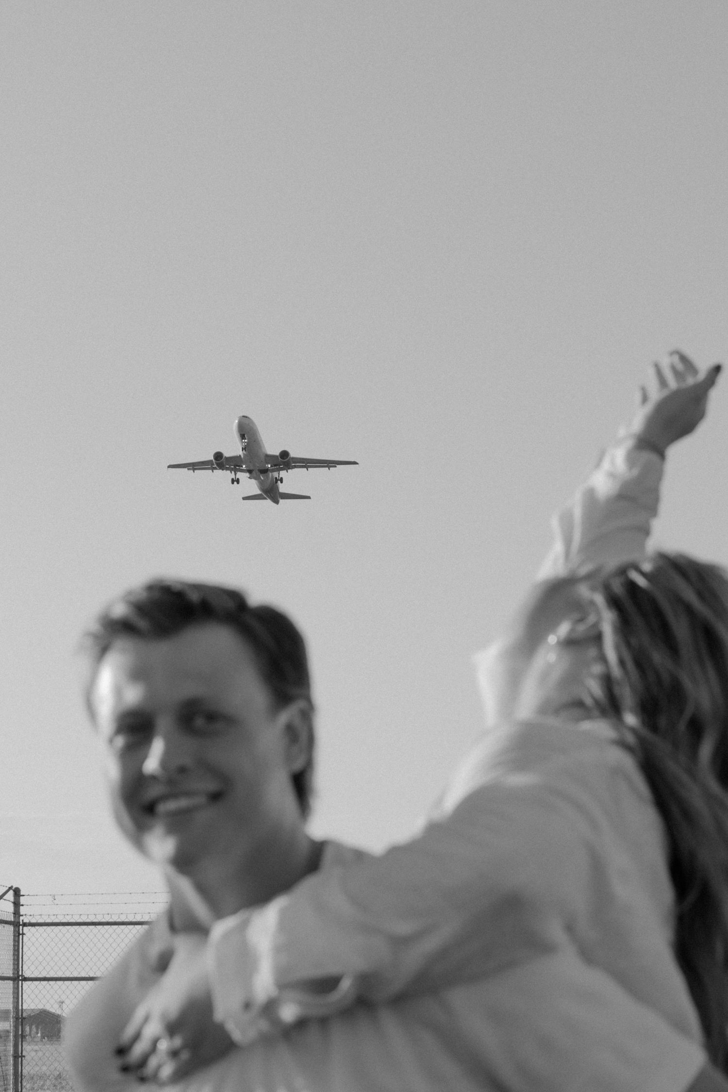 Two people lying in grass watching planes fly overhead against a grey sky.