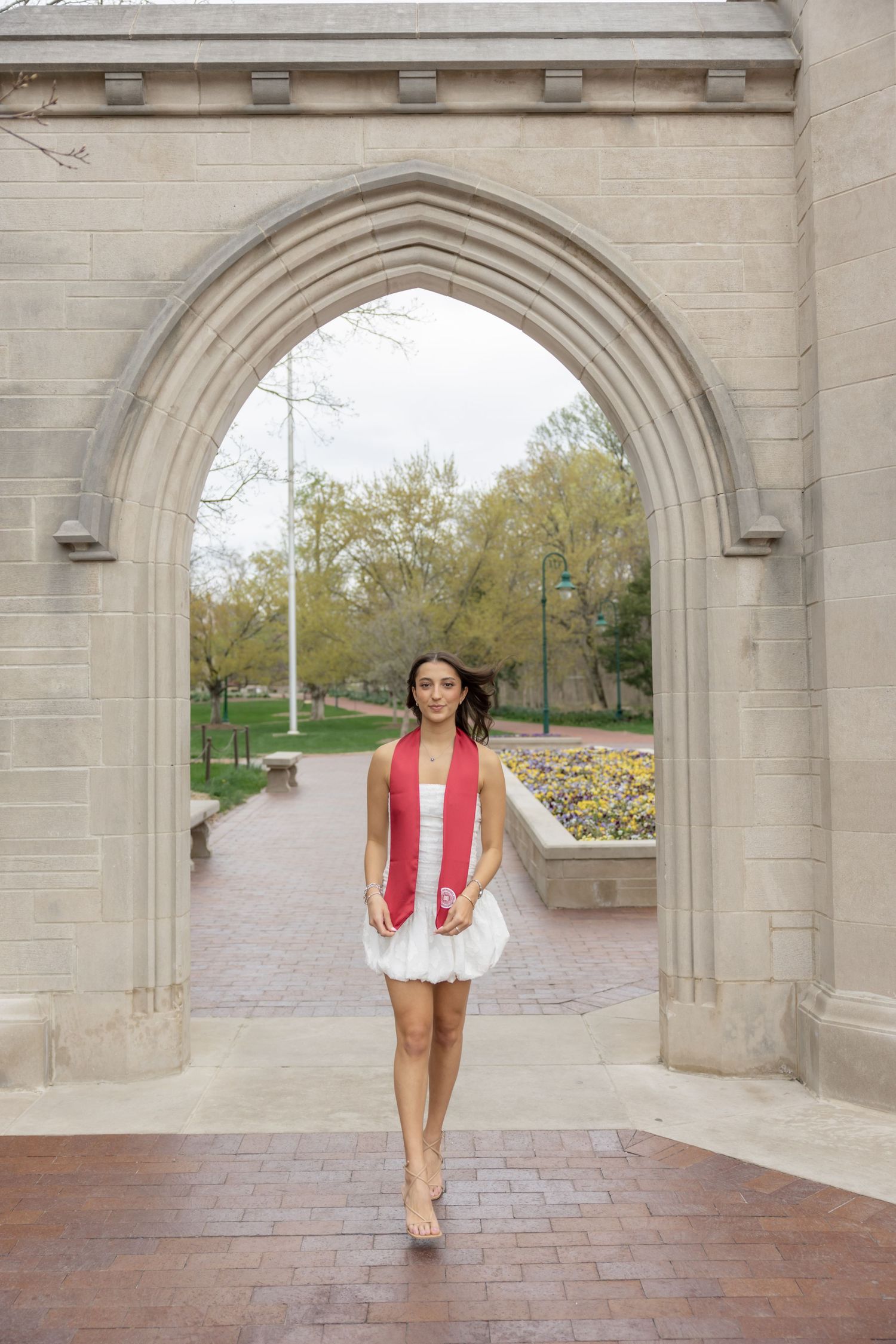 Someone walks beneath gothic stone archways on a brick pathway during a spring day.