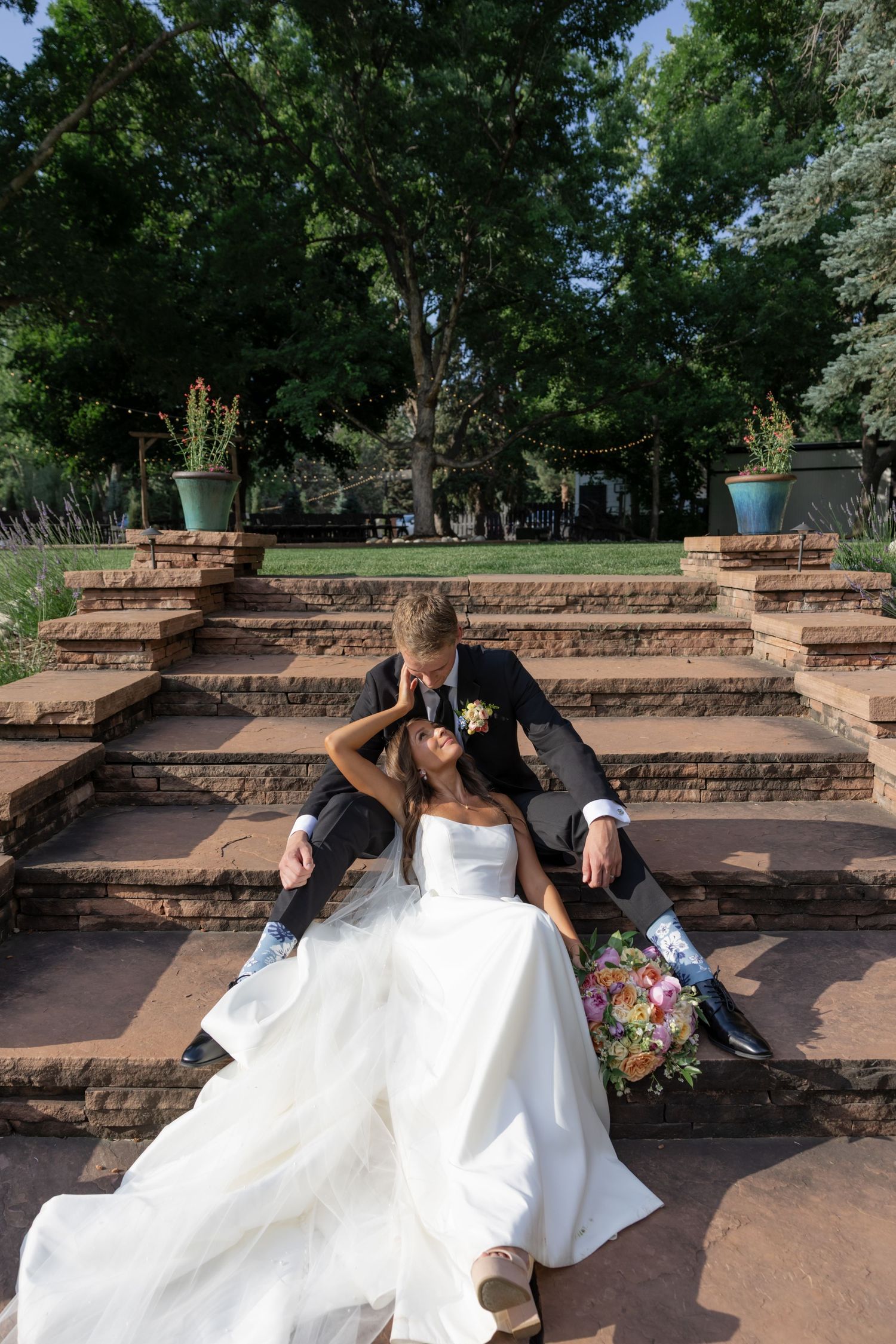 Newlyweds share intimate moment on stone steps surrounded by lush garden.
