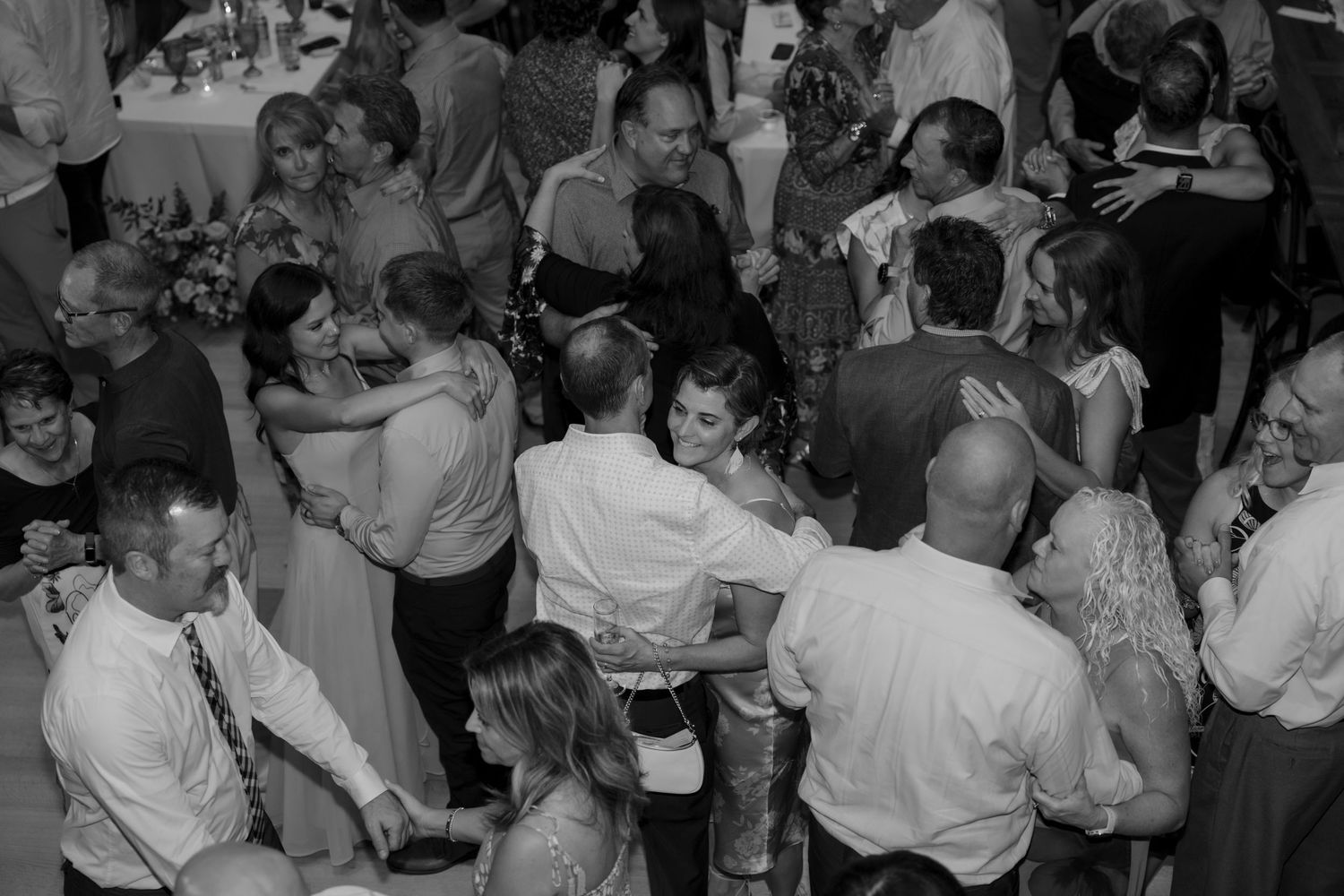 Black and white photo of wedding guests dancing at a lively reception.
