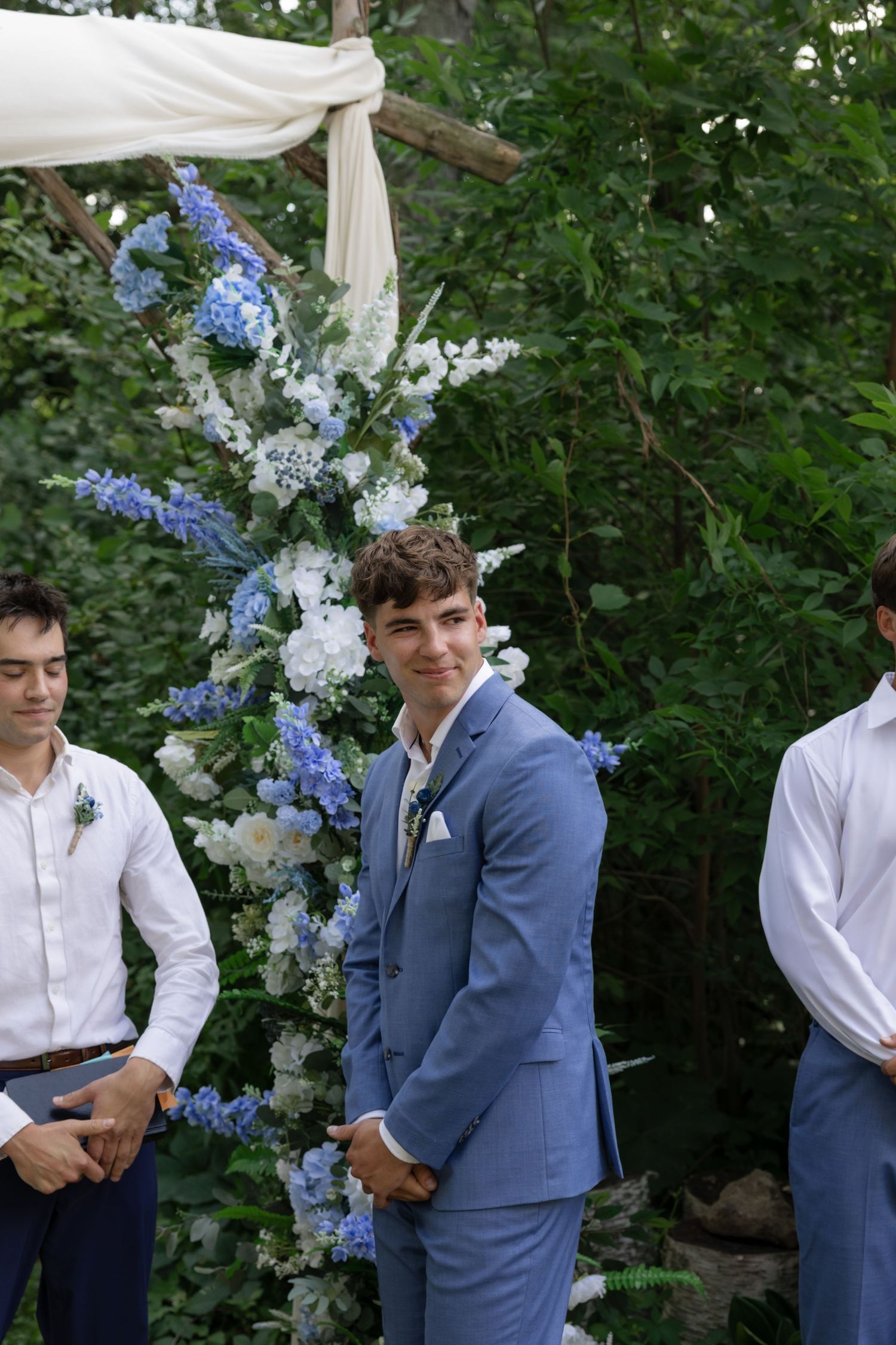 Wedding party members standing near floral arrangements with blue and white flowers.