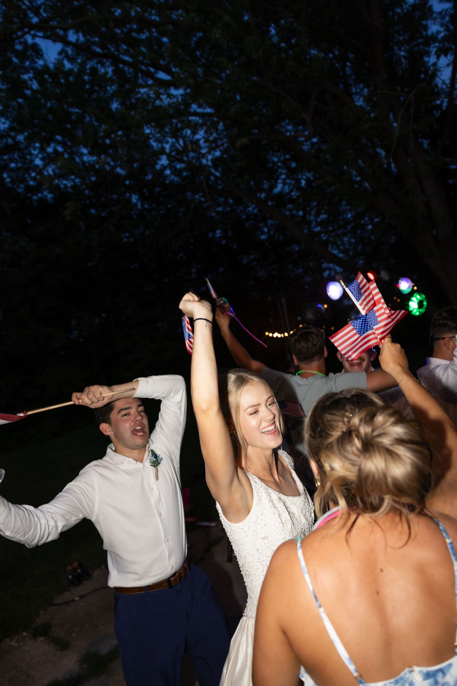 Group celebrating with American flags under dark sky and string lights.