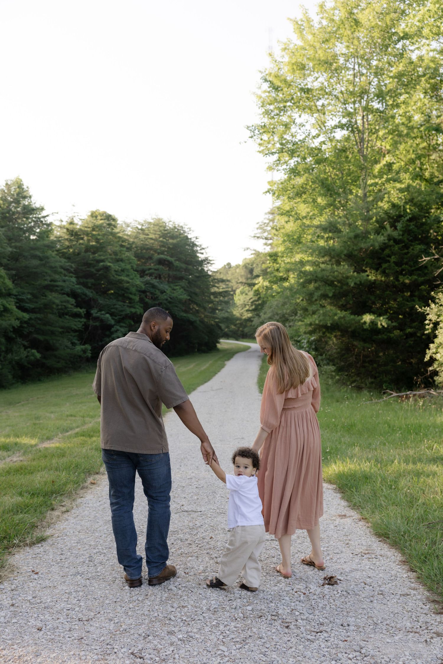 Family walking together on a gravel path surrounded by trees.