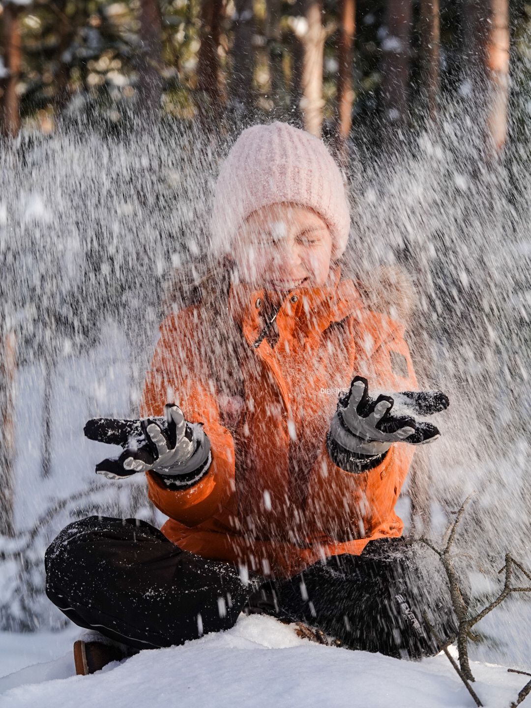Lapsi istuu maassa risti-istunnassa ja heittää eteensä pakkaslunta
