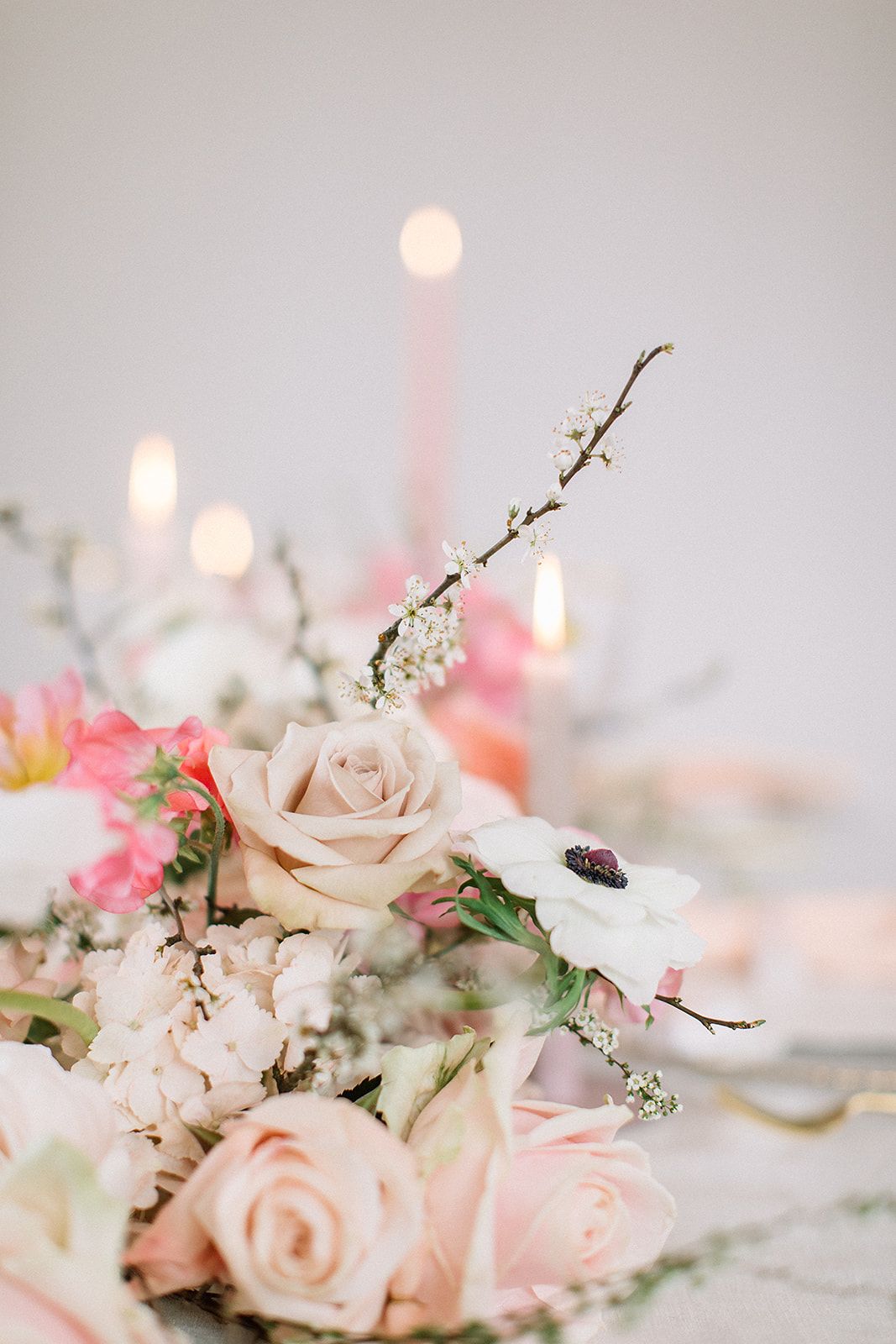 Nahaufnahme eines romantischen Blumenarrangements mit zarten Rosen und weißen Anemonen, umgeben von leuchtenden Kerzen