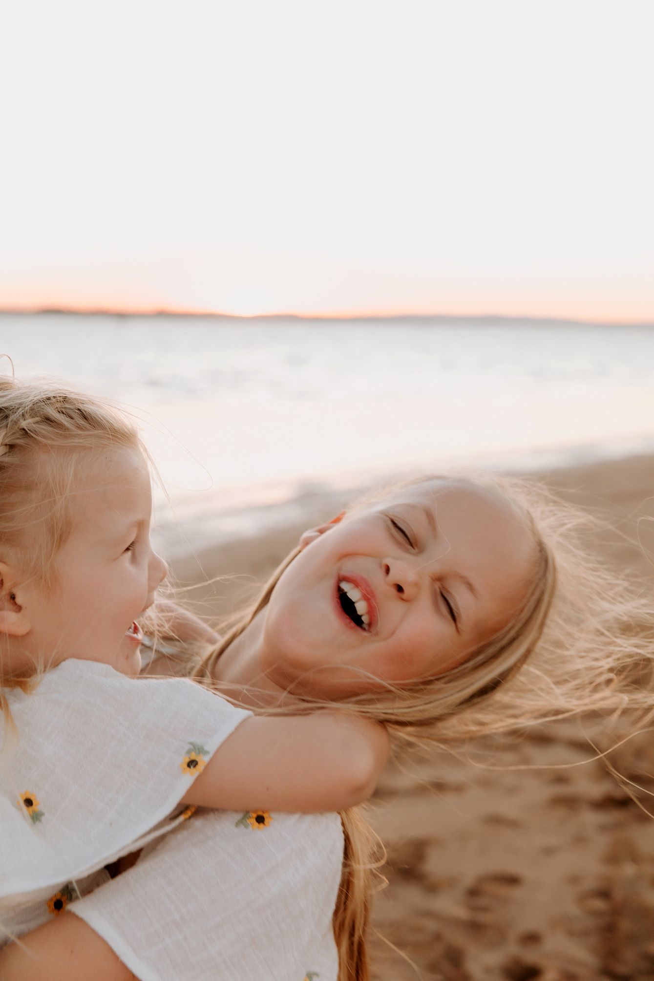 Children playing and laughing on sandy beach at sunset.